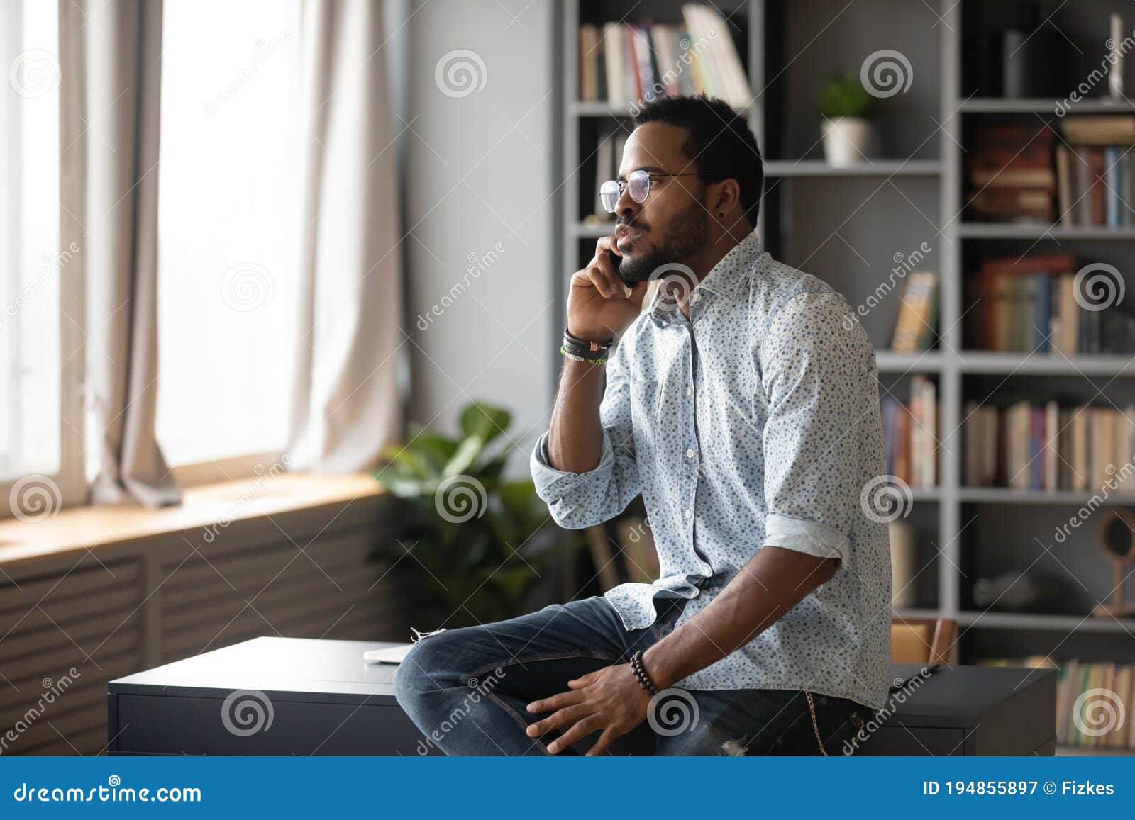 serious african american man talking on phone, sitting on desk