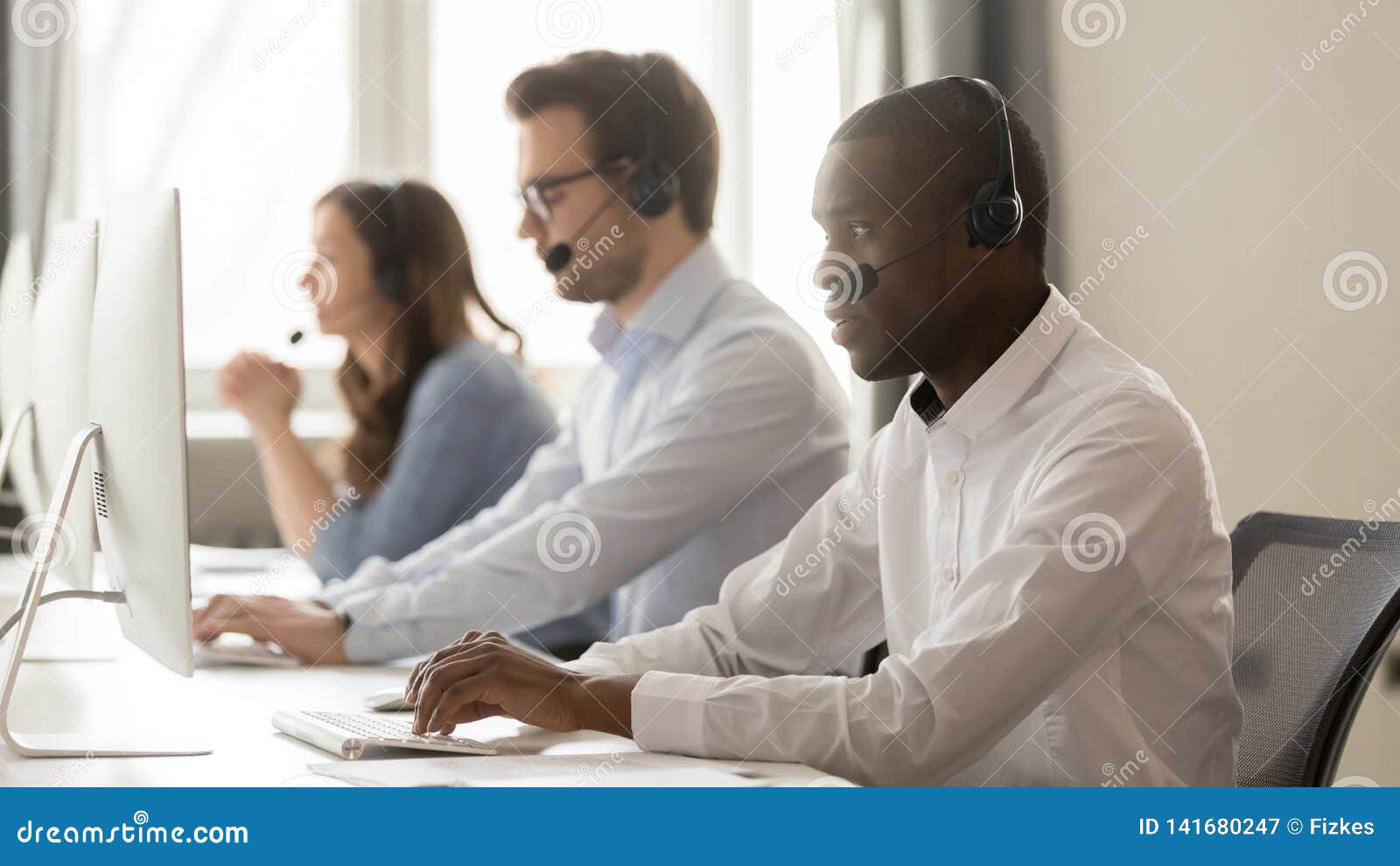 serious african call center agent in headset working on computer