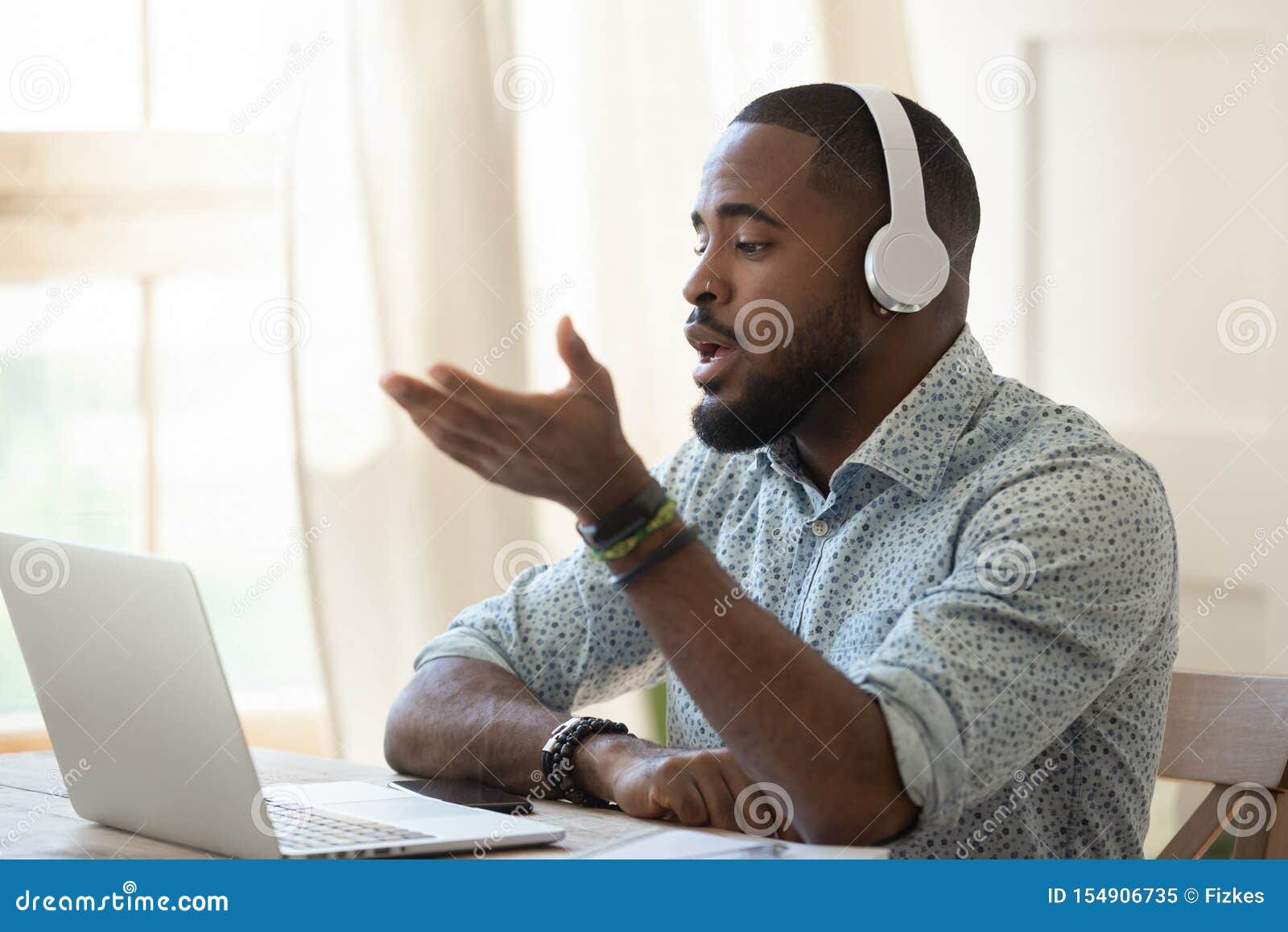 african male skype teacher wearing headphones talking looking at laptop