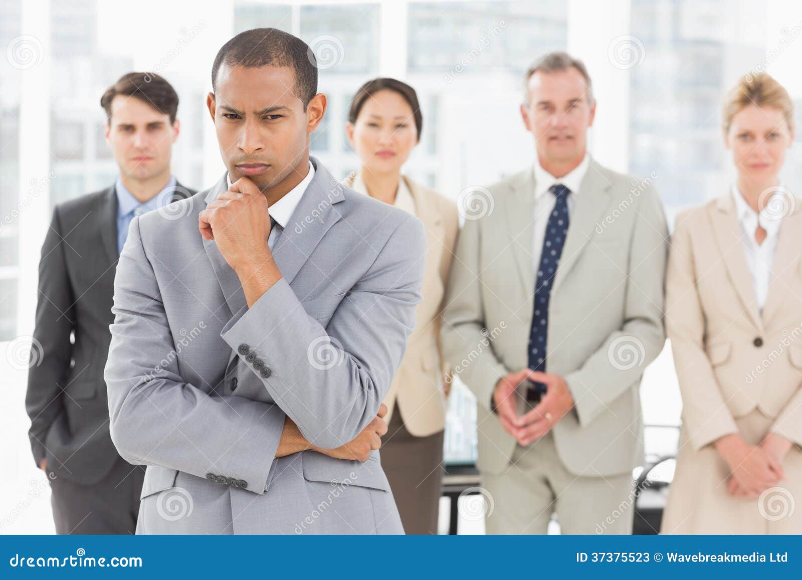 Serious businessman frowning at camera with team behind him in the office