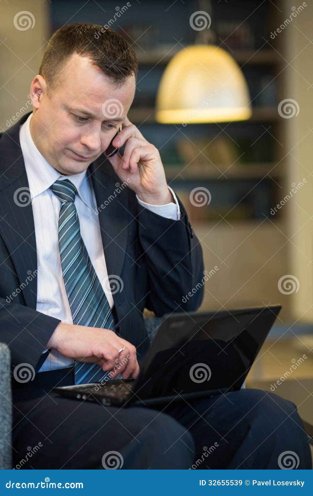 Serious businessman in suit and tie sitting with a laptop. Serious businessman in suit and tie sitting on a chair with a laptop and talking on the phone