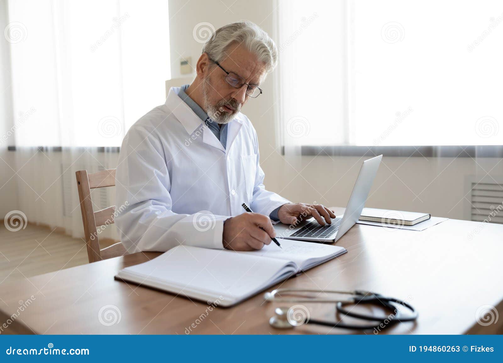 Serious Busy Mature Doctor Filling Documents, Sitting at Work Desk ...