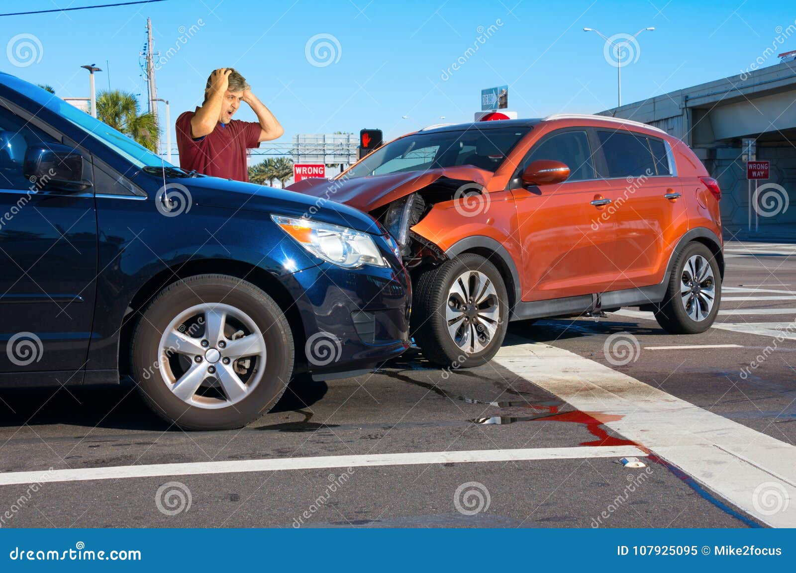 serious bad car wreck at intersection with very upset man driver looking at damage