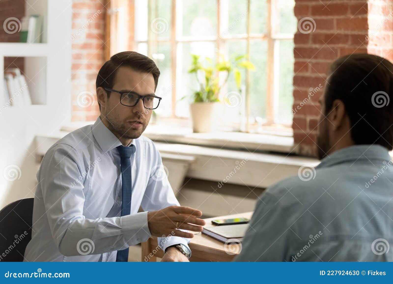 serious male colleagues discuss business seated at workplace desk