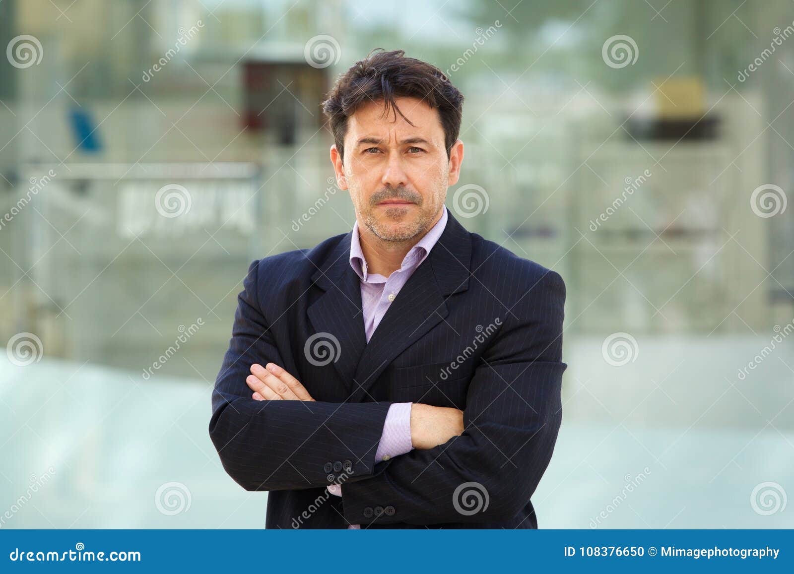 serious older man in business suit standing with arms crossed outdoors