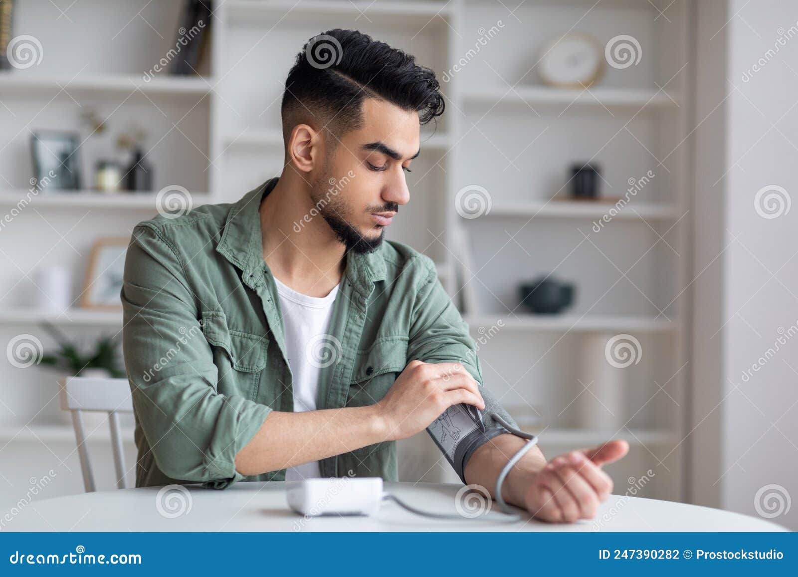 serious sad young middle eastern man with beard measures blood pressure with tonometer, feels bad