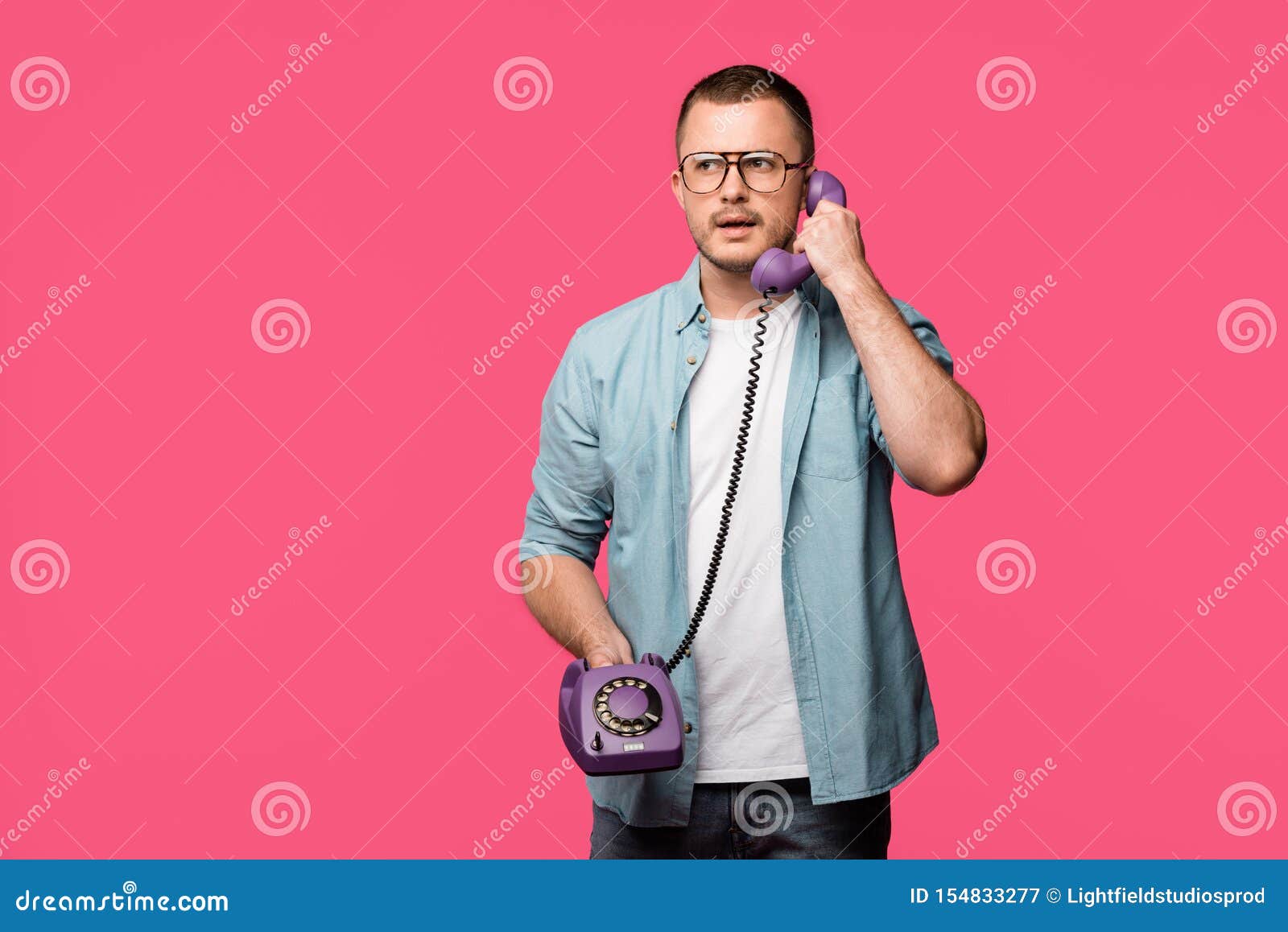 serious young man in eyeglasses talking by vintage telephone 