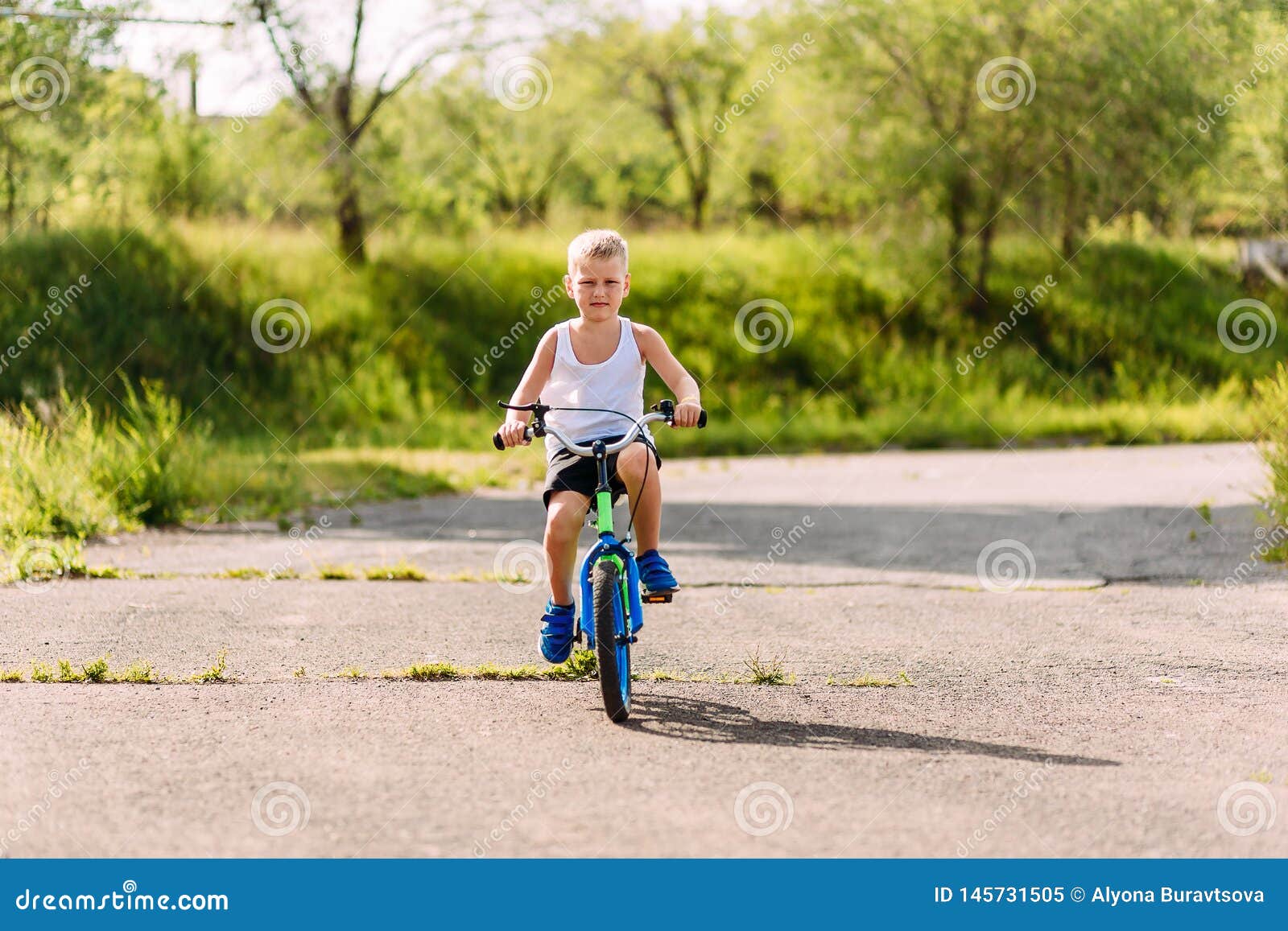 seven-year-old boy in a white t-shirt rides a children`s blue bike outdoors in the summer