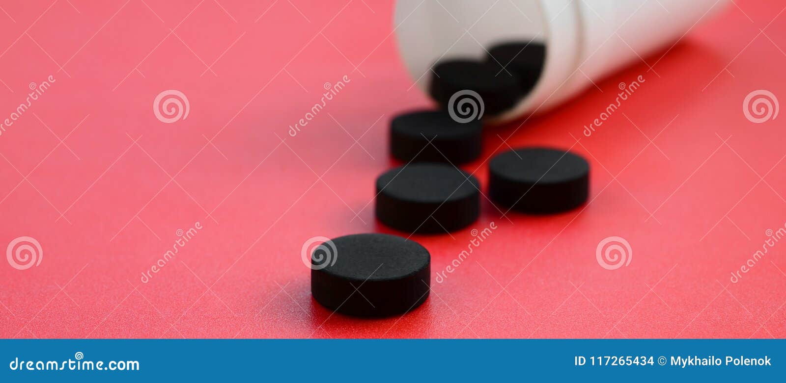 Several Black Tablets Fall Out of the Plastic Jar on the Red Surface