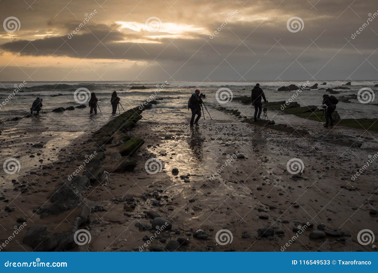 several photographers `fish` photos on the rocky beach at sunset