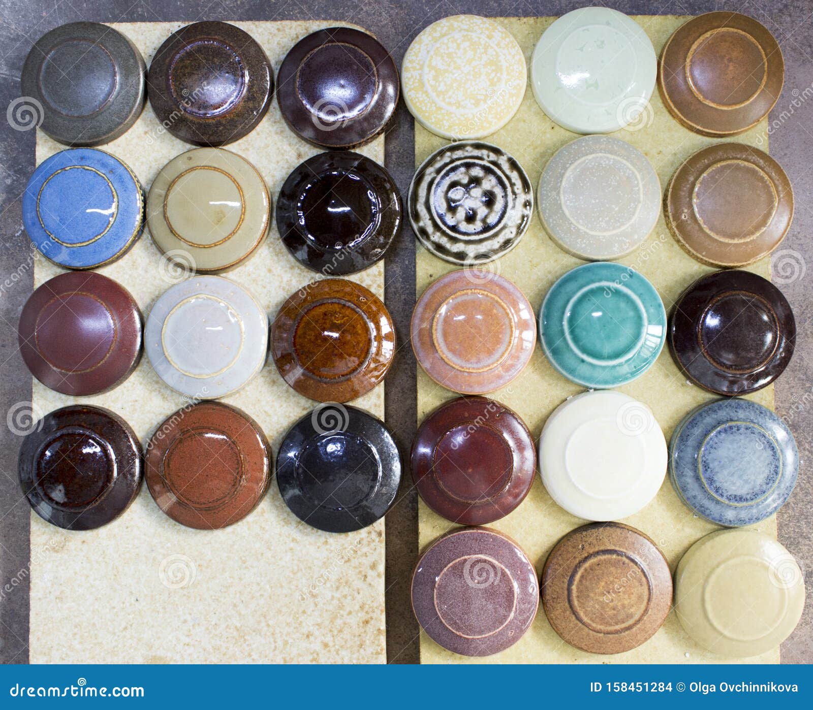 several round clay samplers with multi-colored glazes on them lie on the square stones after firing