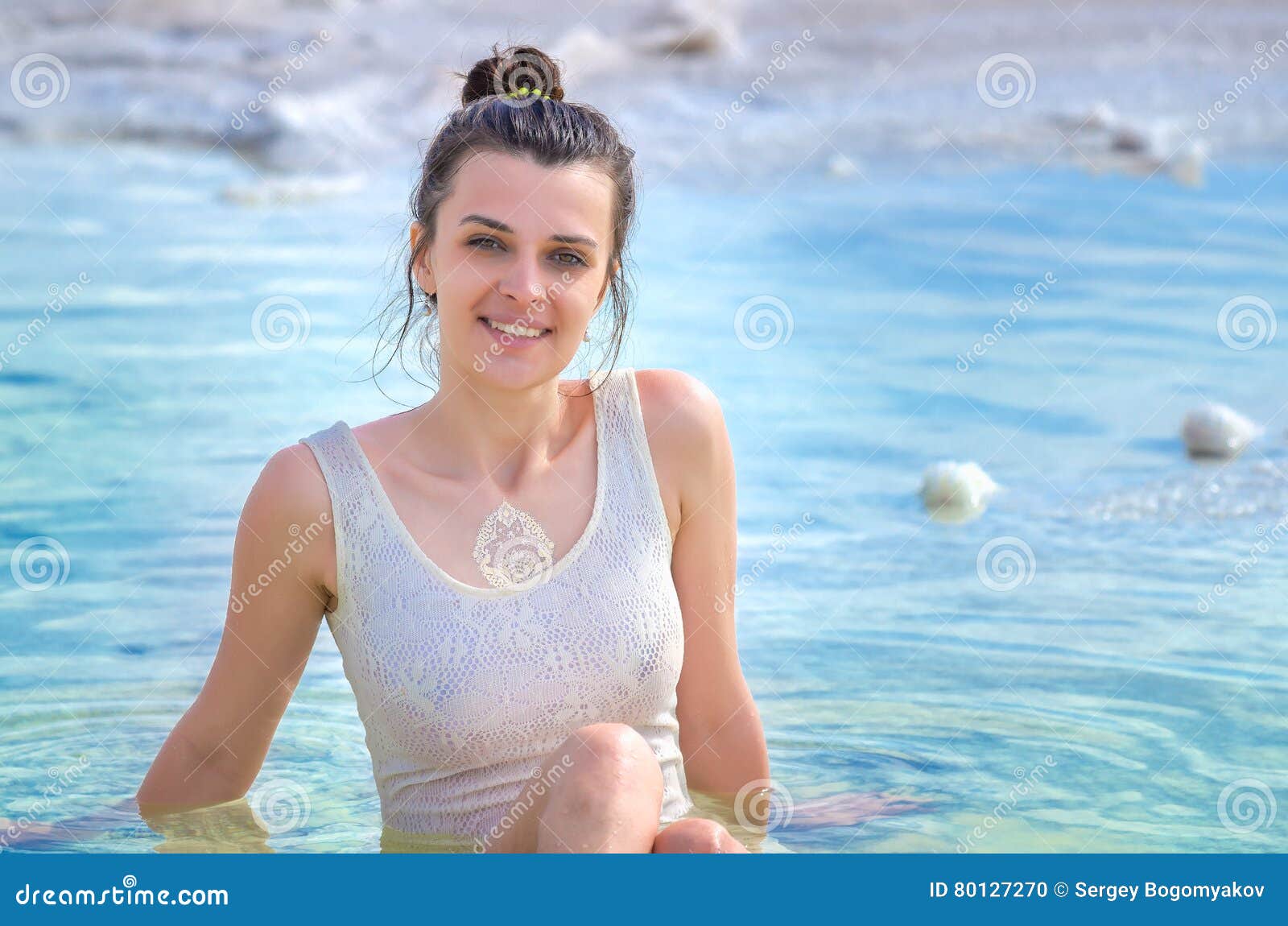 Attractive Girl Wears White Dress Sits in Water and Looks To