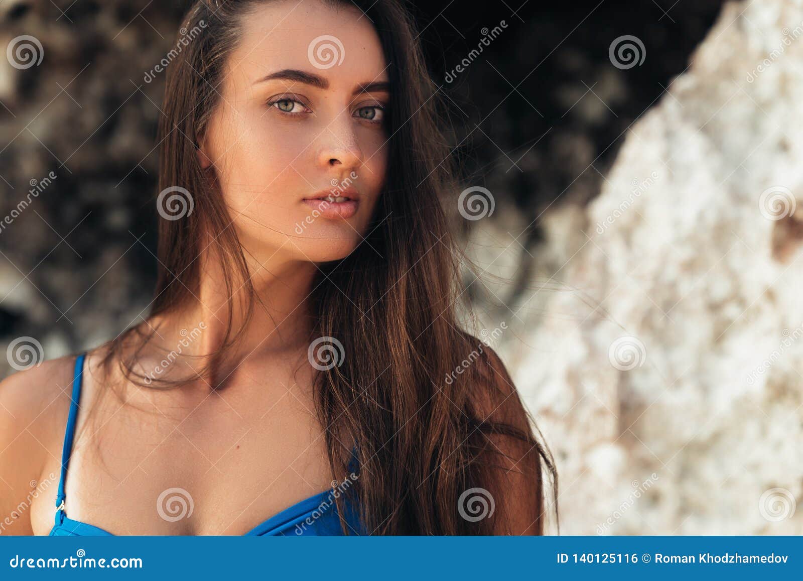 Brunette Girl In Blue Swimsuit Sunbathes On The White Sand Beach Near