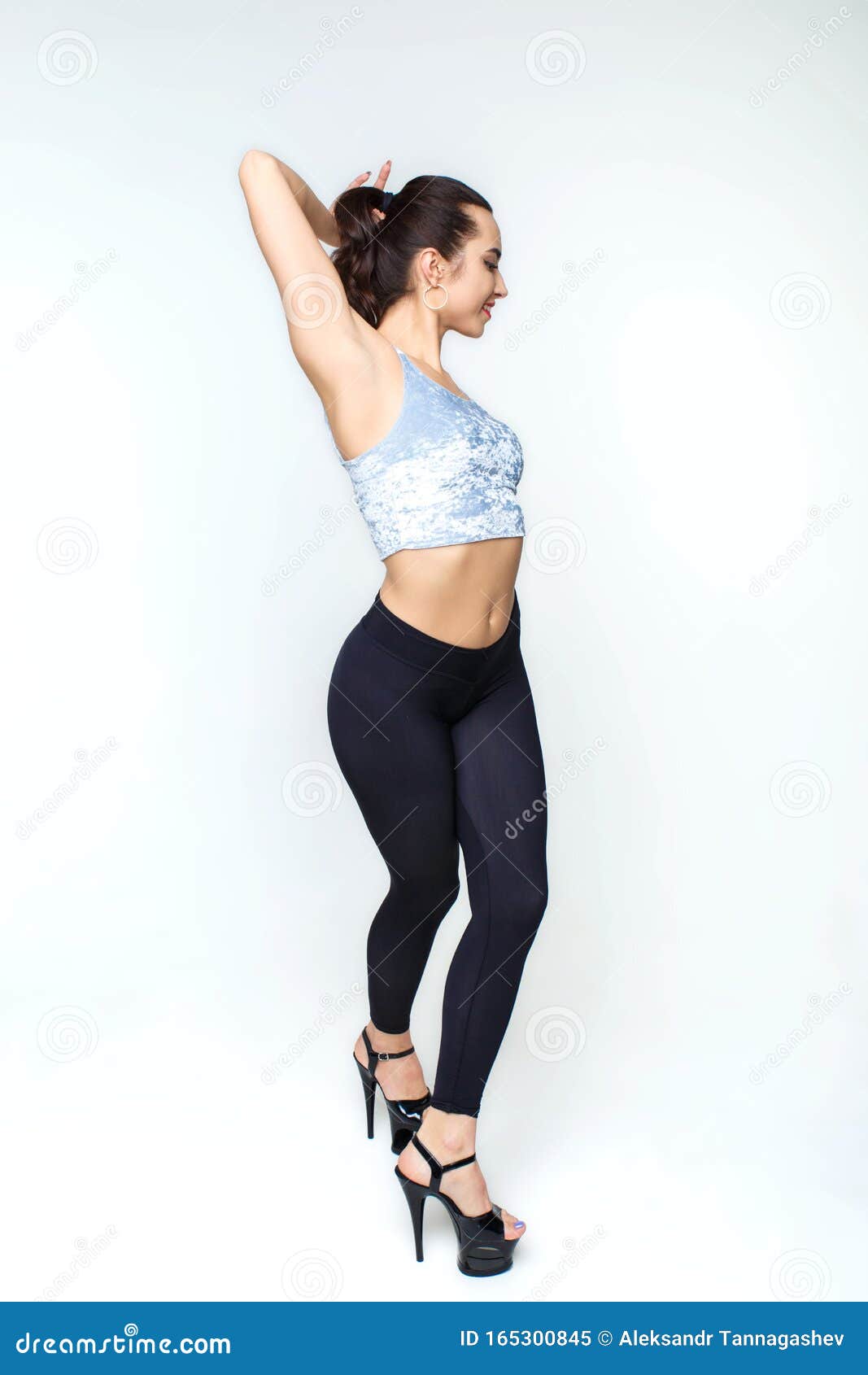 Cute athletic young beautiful woman dancer in stylish black leggings in a  black pullover in black sports sneakers posing in a studio near a white  wall. Attractive girl Stock Photo