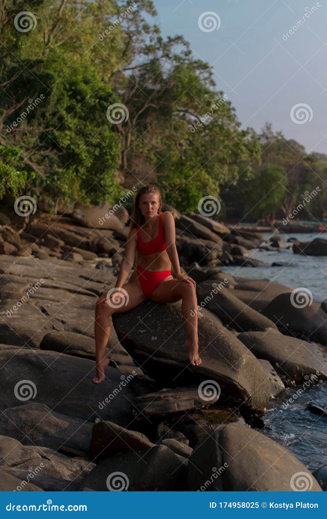 Tanned Brunette In Red Bikini Sitting On The Stone Among Tropical Beach 