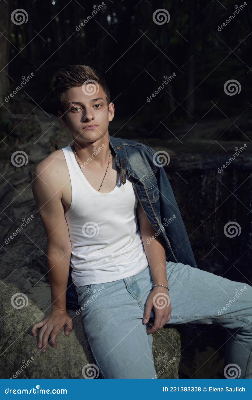 Trendy Teen Guy in a White T-shirt and Blue Jeans is Sitting on a Rock ...