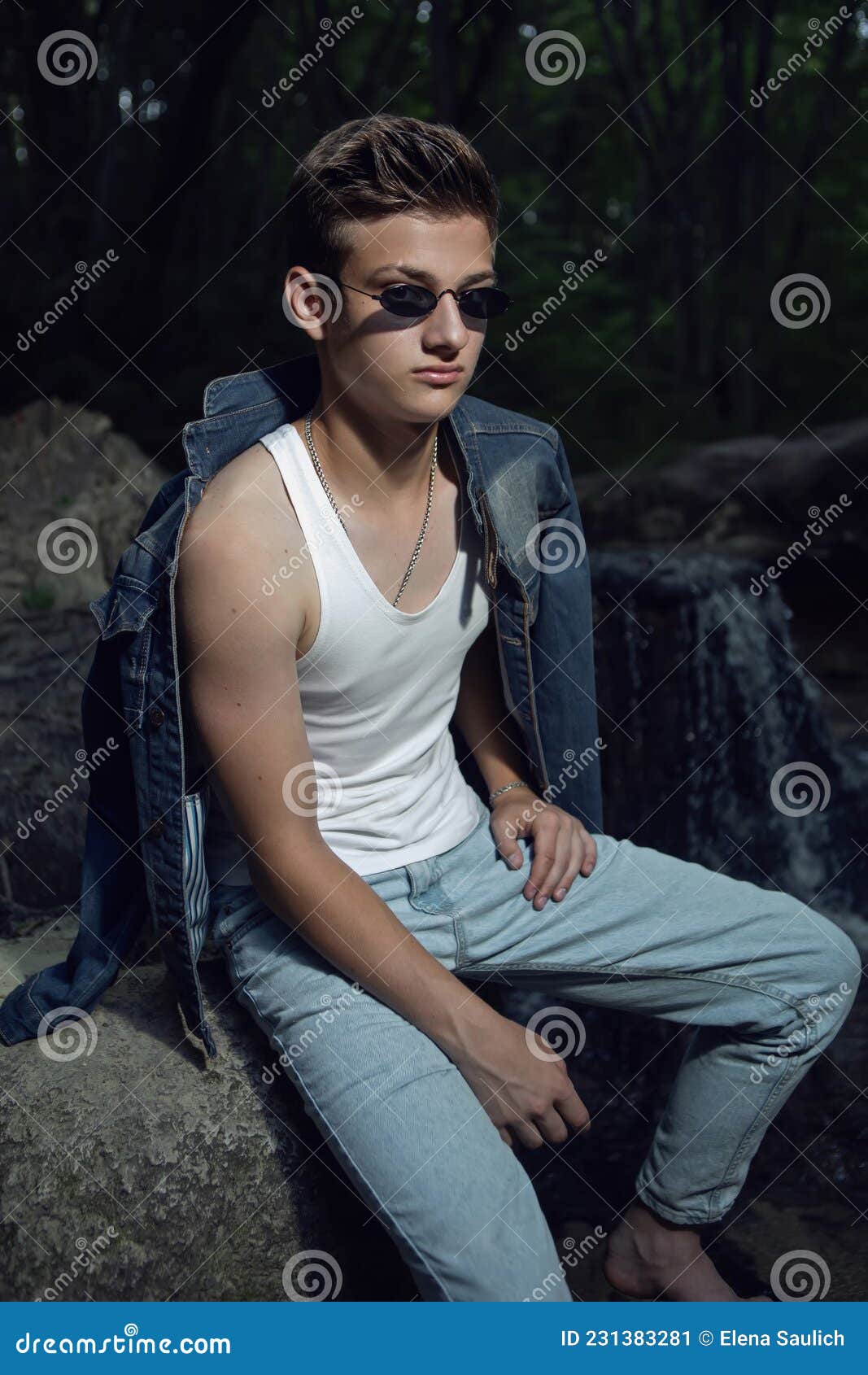 Trendy Teen Guy in a White T-shirt and Blue Jeans is Sitting on a Rock ...