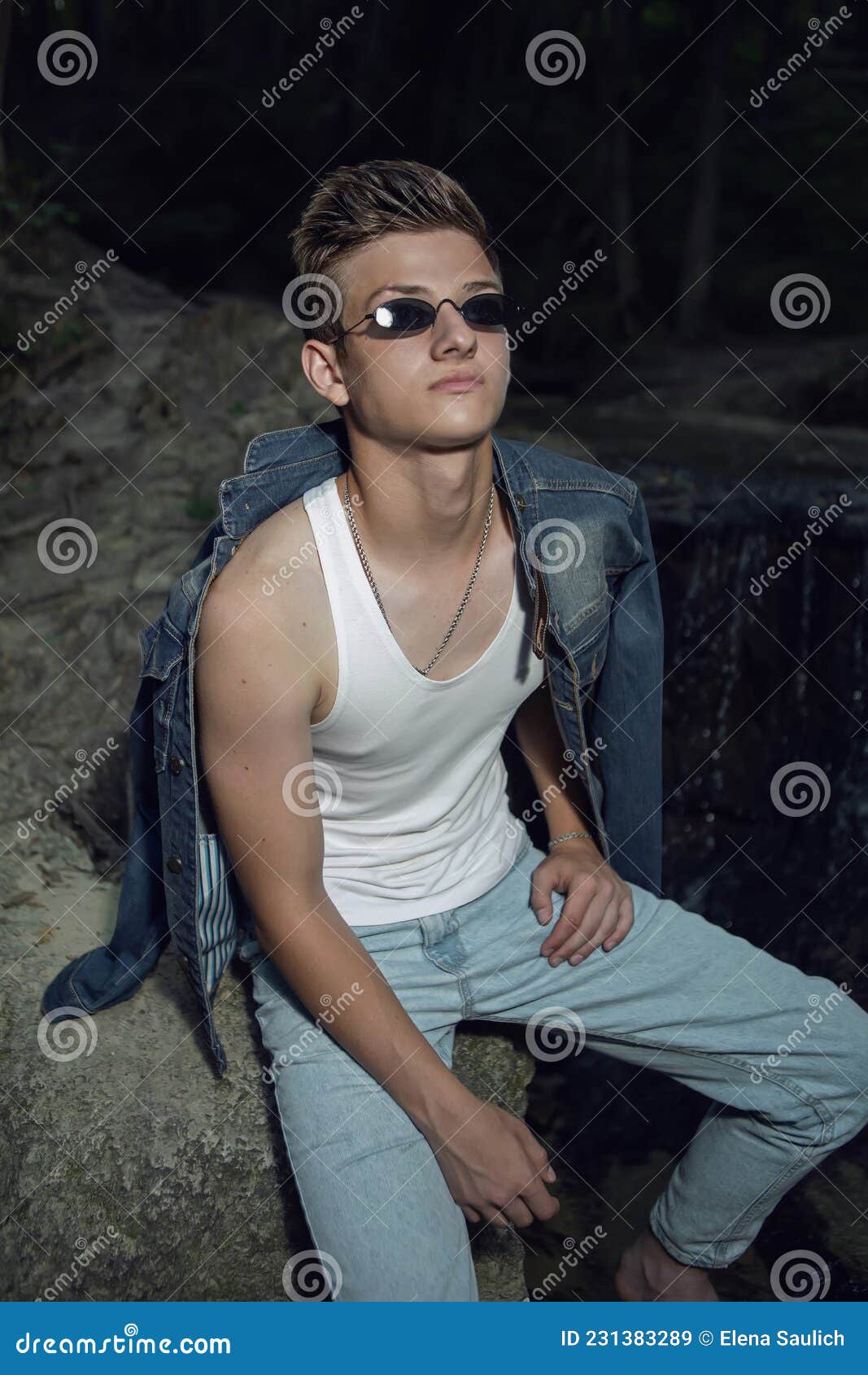 Trendy Teen Guy in a White T-shirt and Blue Jeans is Sitting on a Rock ...