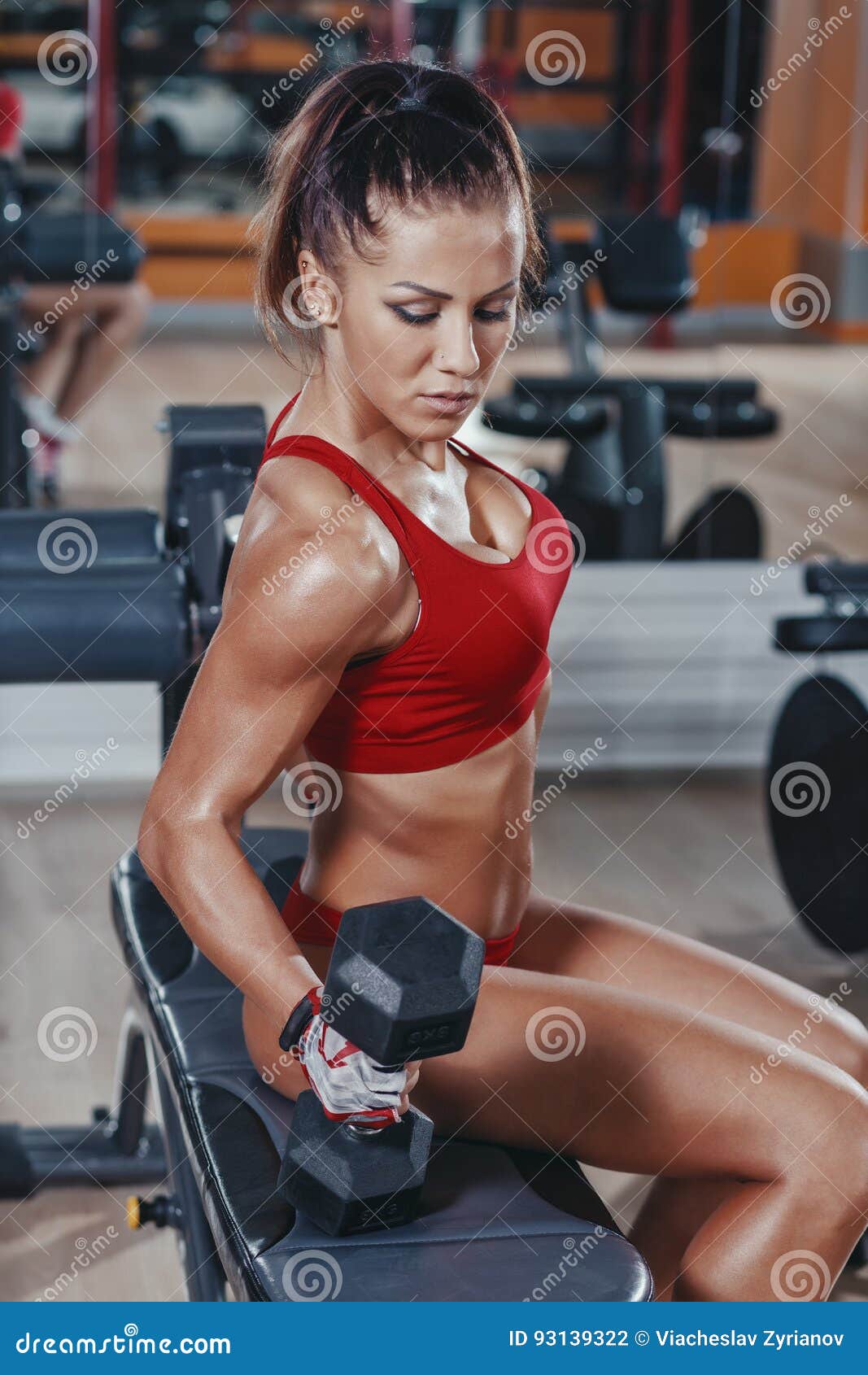 Young Woman Exercising Biceps With Dumbbells In The Gym And