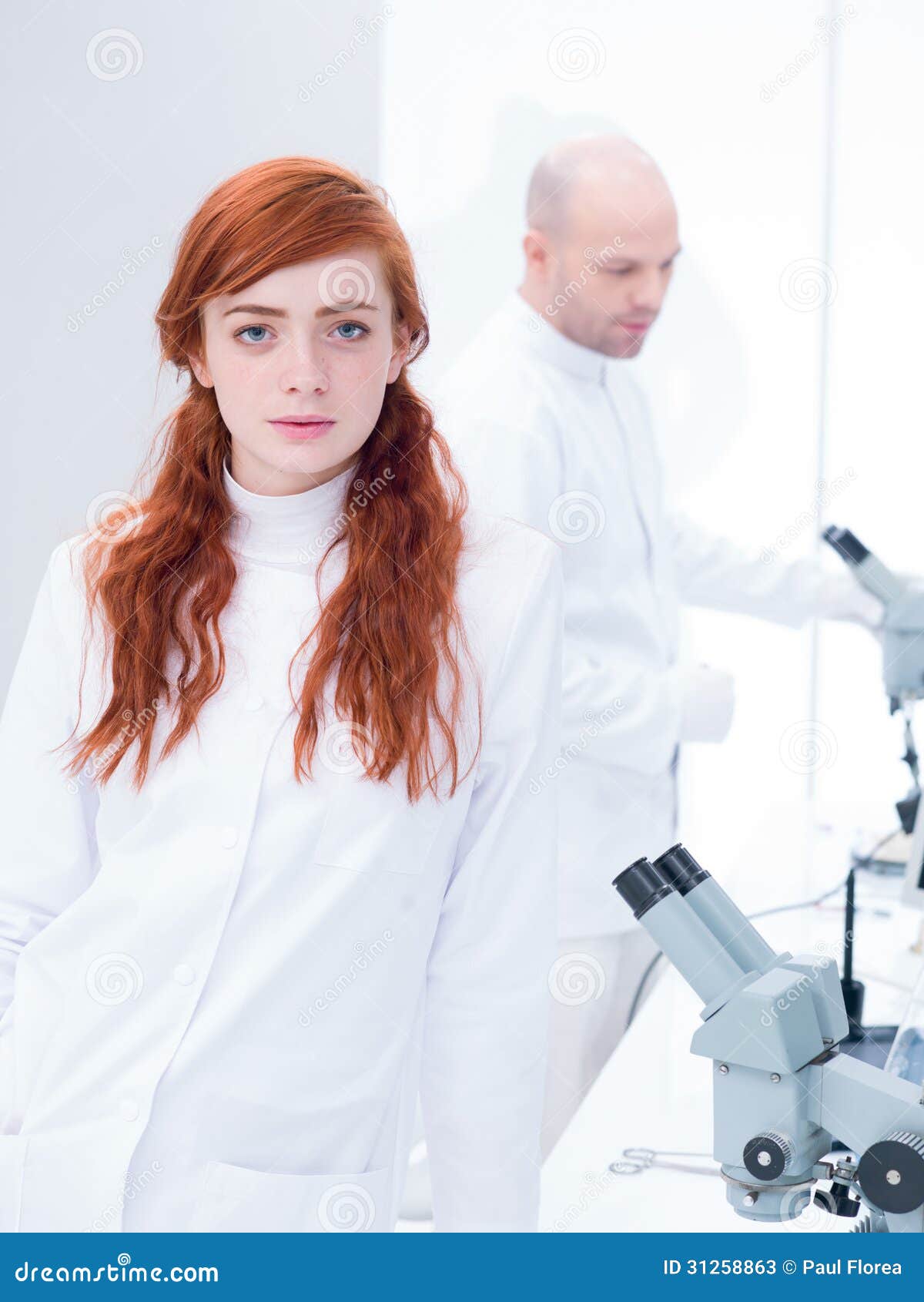 Sguardo dello studente in un laboratorio di chimica. Generale-vista di uno studente attraente in un laboratorio di chimica che guarda nella macchina fotografica con il suo insegnante che analizza sotto il microscopio sui precedenti