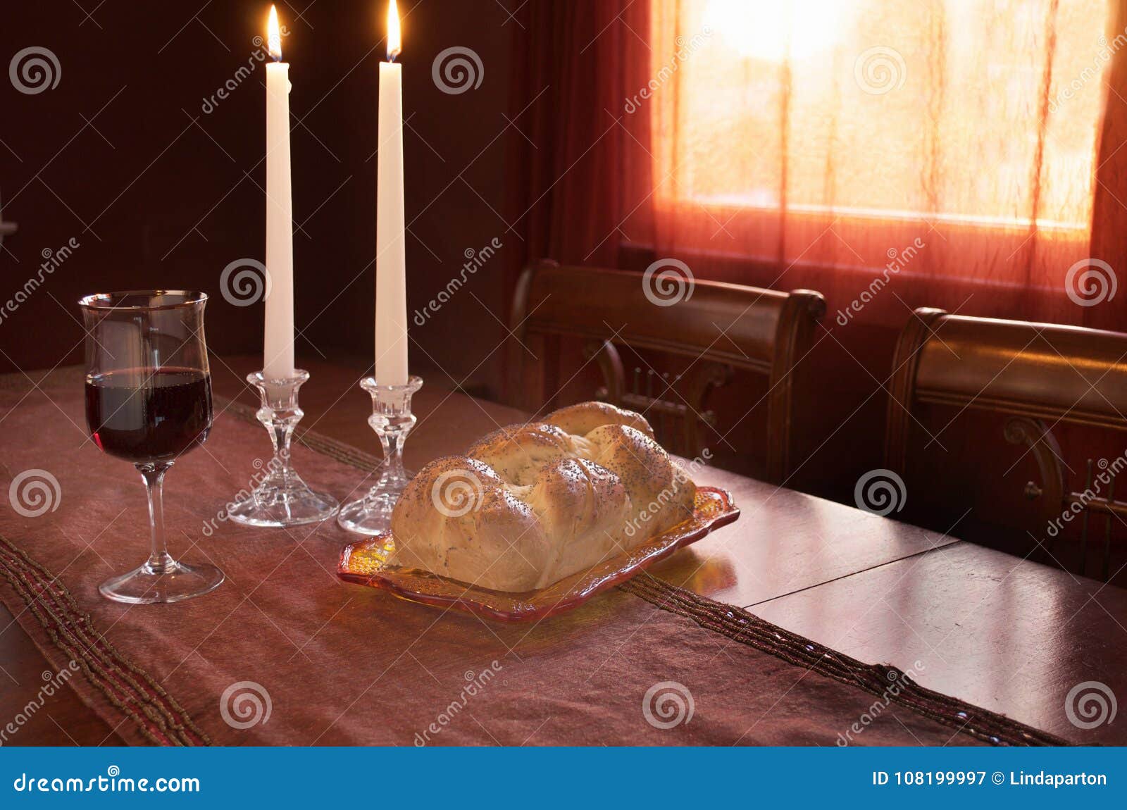 shabbat observance at sunset: challah, glass of wine, two lit candles