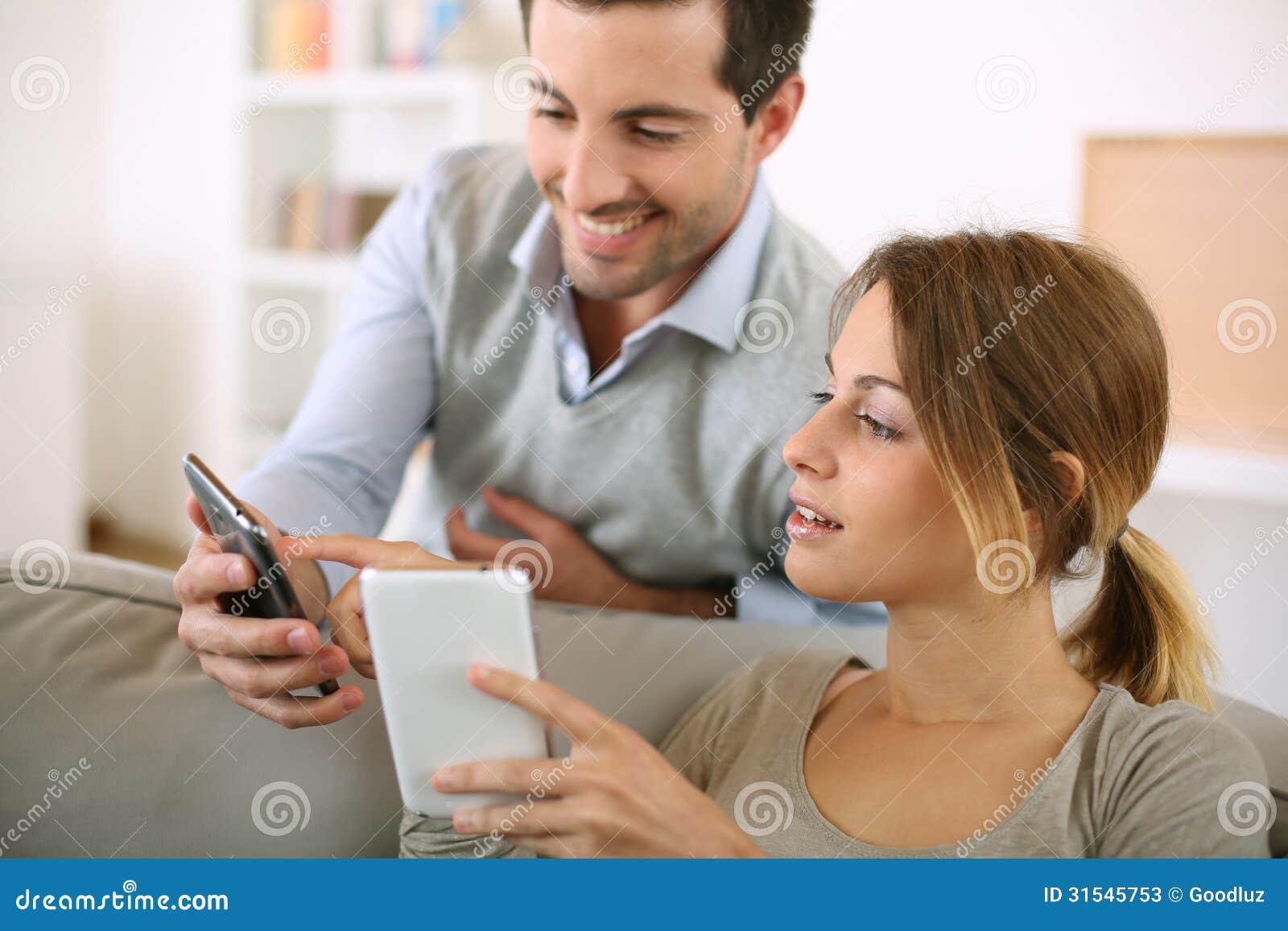 Sharing data with electronic devices. Young couple using smartphone at home