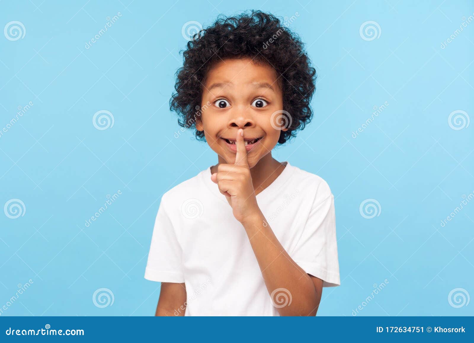 shh, be quiet! portrait of funny cute little boy with curly hair in t-shirt making silence gesture with finger on his lips