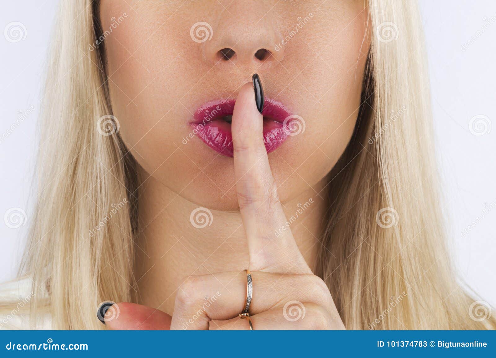 shh! women`s secrets. beautiful blond woman holding her finger to her pink lips in a gesture for silence. making silence sign with