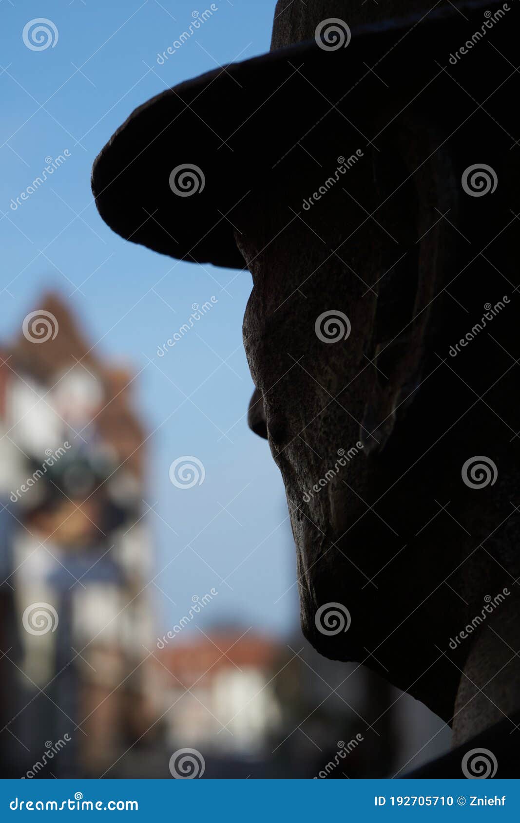 shilouette of the head of a sculpture against a blurred background with the view of buildings of a city