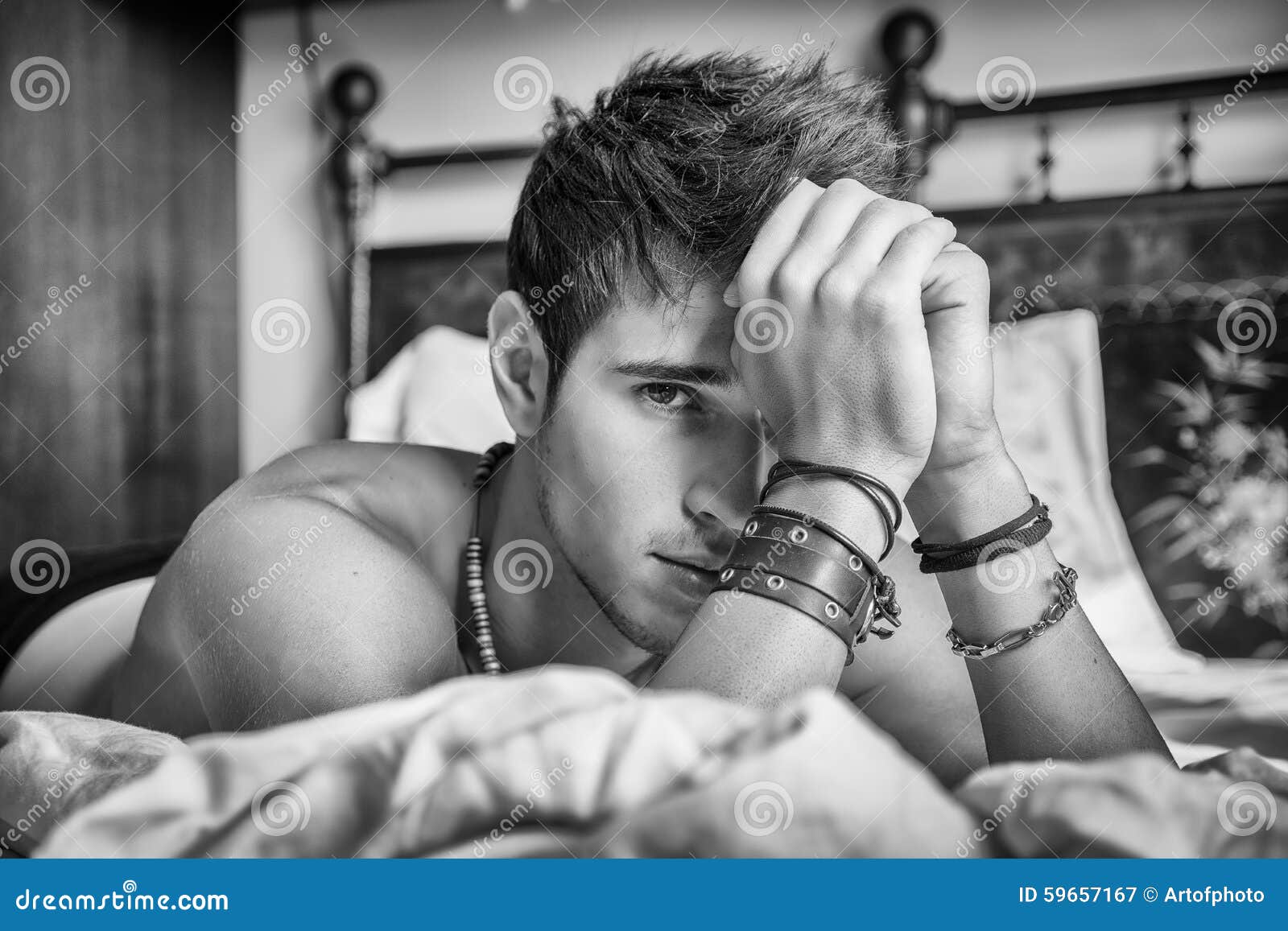 Shirtless Male Model Lying Alone On His Bed In His Bedroom Looking At The Camera With A