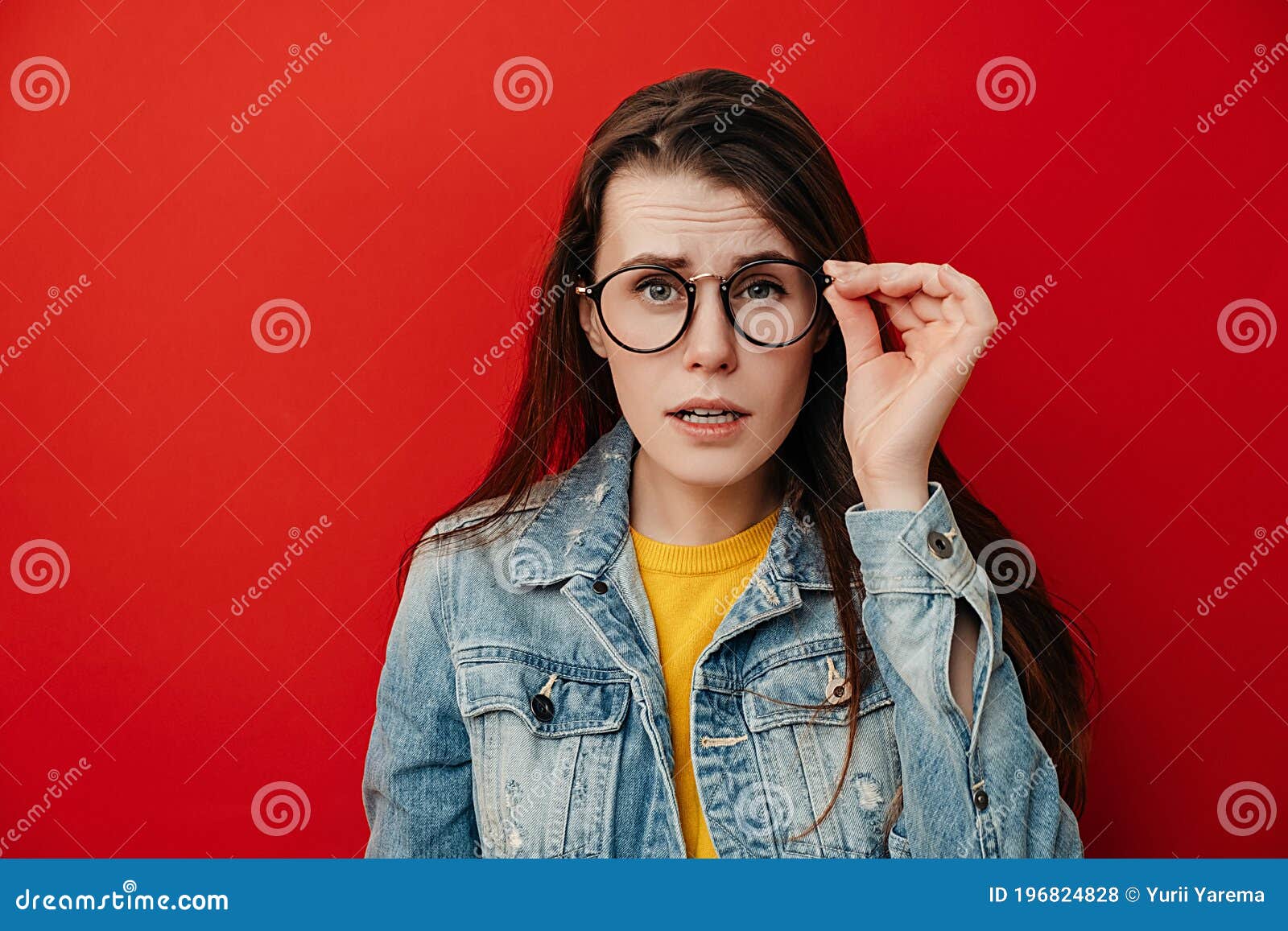 Shocked Emotional Young Woman Keeps Hand On Rim Of Spectacles Dressed