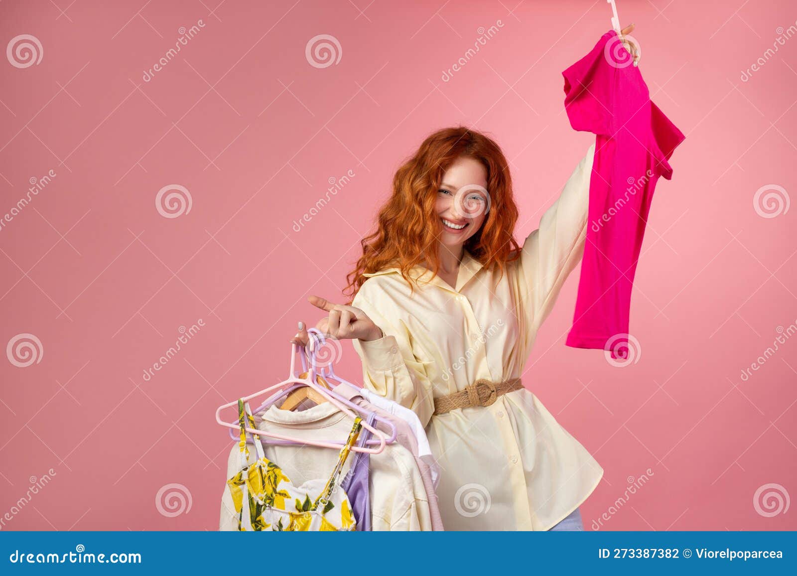 shopaholic young woman holding clothes and shooping bags on pink background.