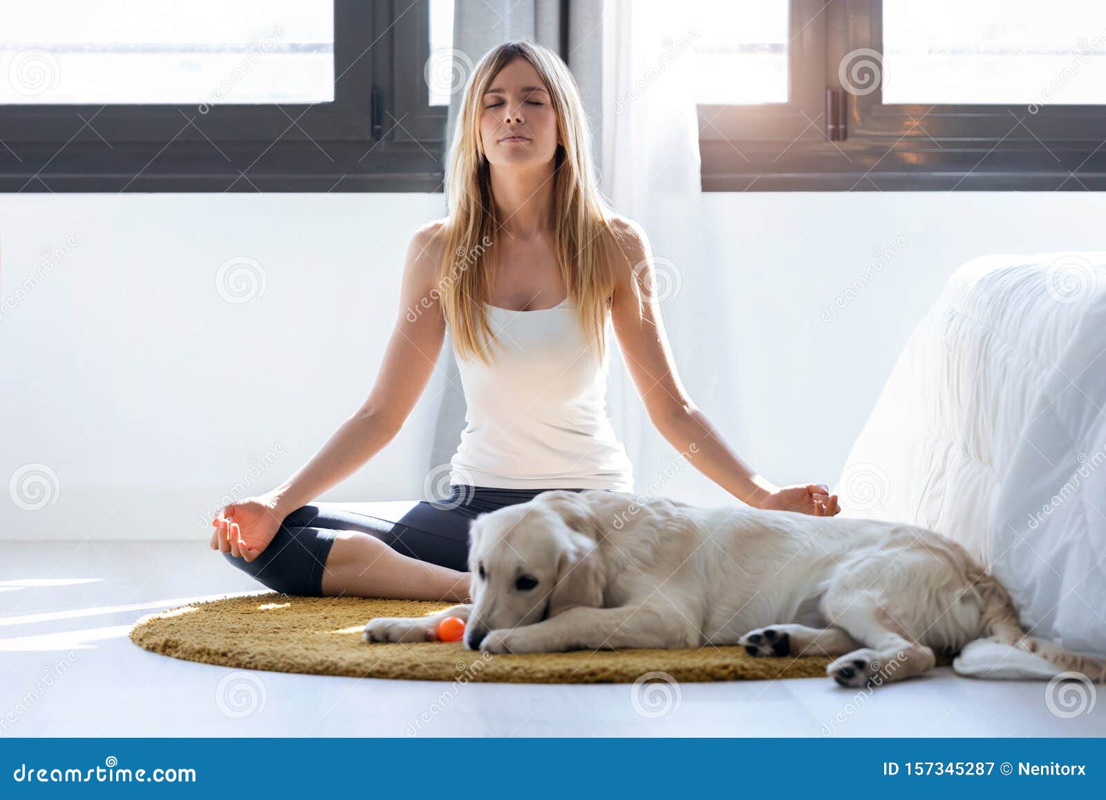 pretty young woman doing yoga while her dog lying on the floor at home