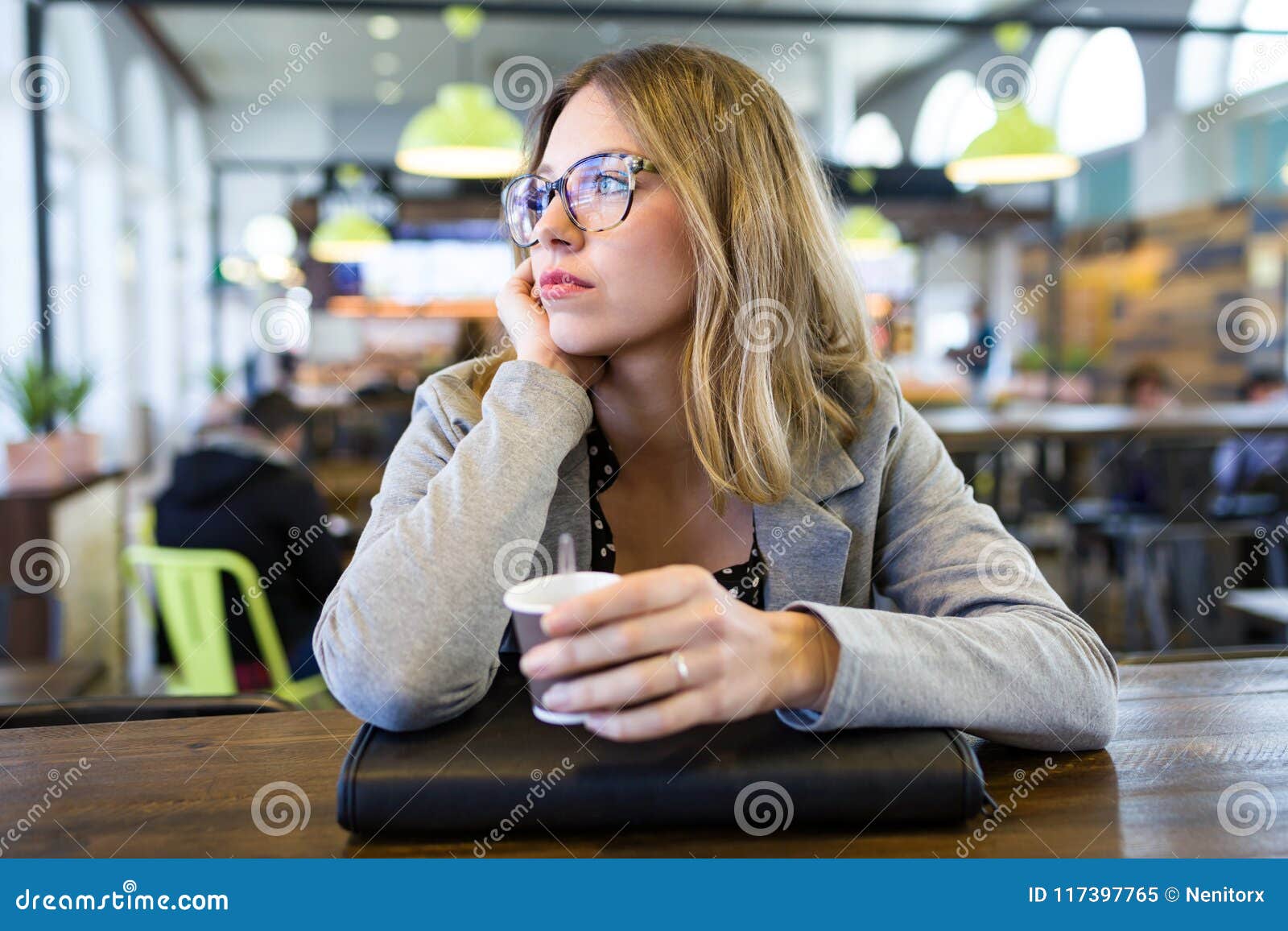 pretty young woman looking sideways while drinking cup of coffee at cafe.