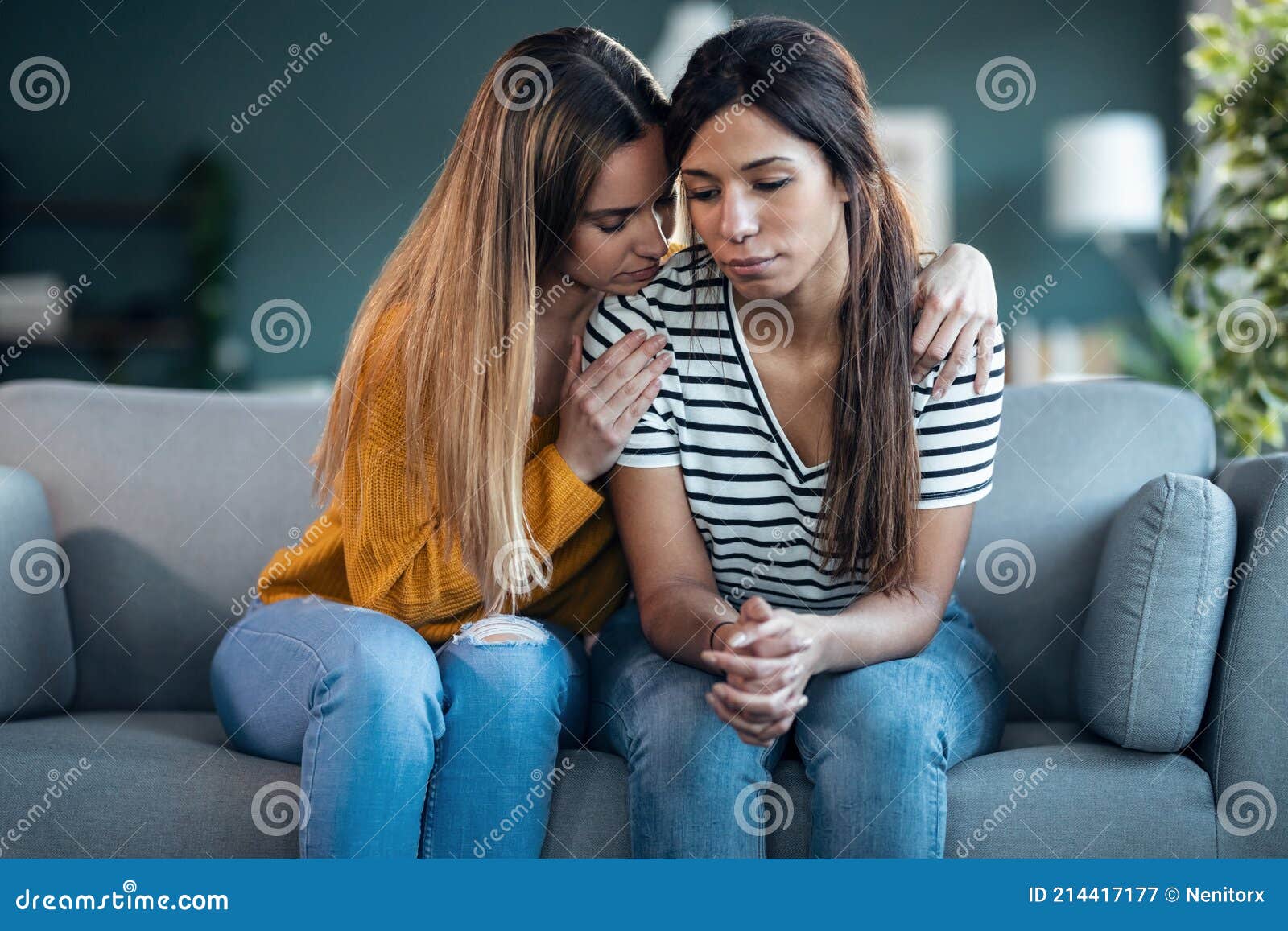 pretty young woman supporting and comforting her sad friend while sitting on the sofa at home