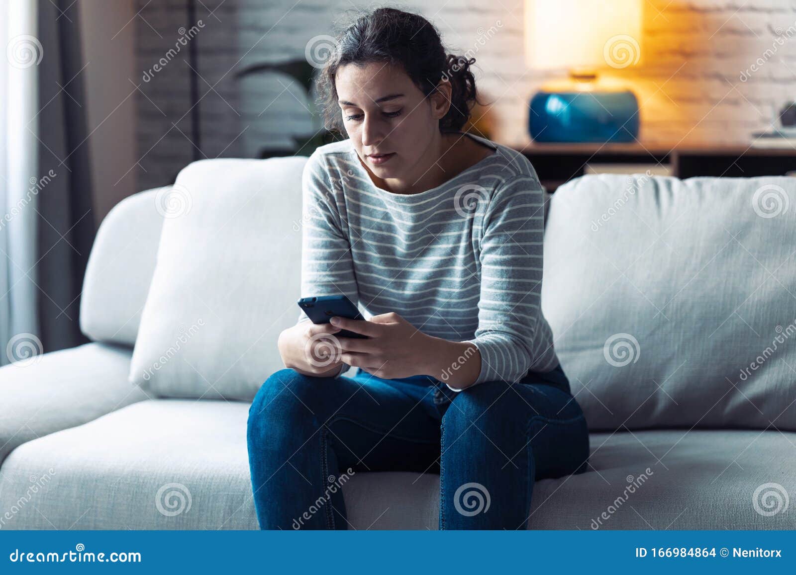 serious young woman using her mobile phone while sitting on sofa in the living room at home