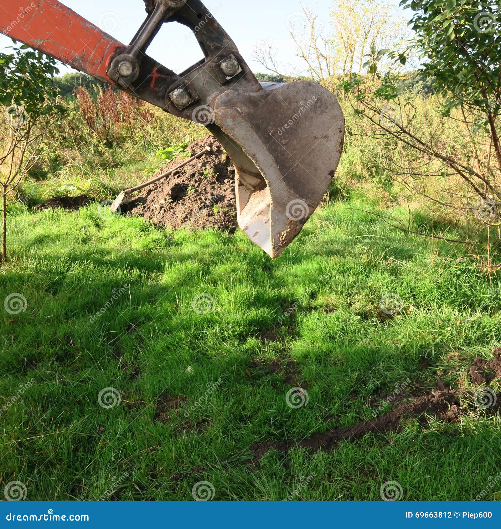 The Shovel of a Mini Digger in the Meadow while Working in Summer Stock