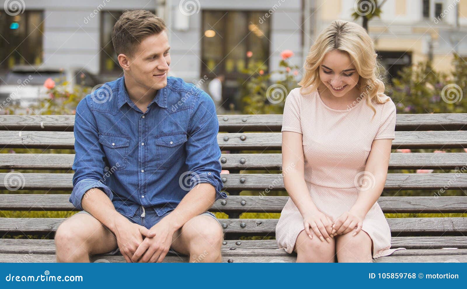 shy blonde girl smiling, attractive guy flirting with beautiful woman on bench