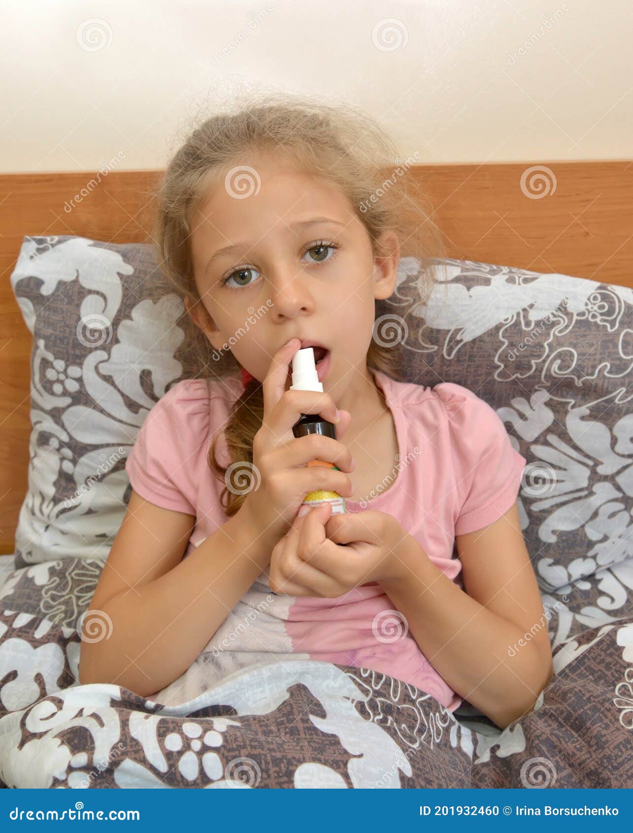 a sick girl holds a spray in her hands and irrigates their throats while sitting in bed. self-treatment