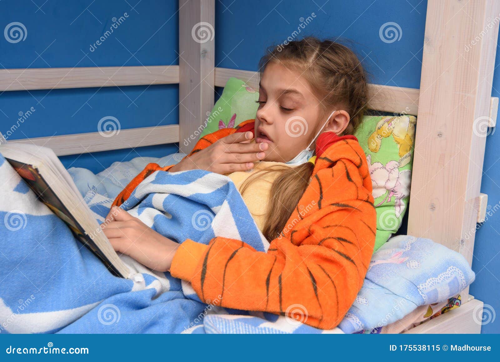 sick girl sneezes lying in bed and reading a book