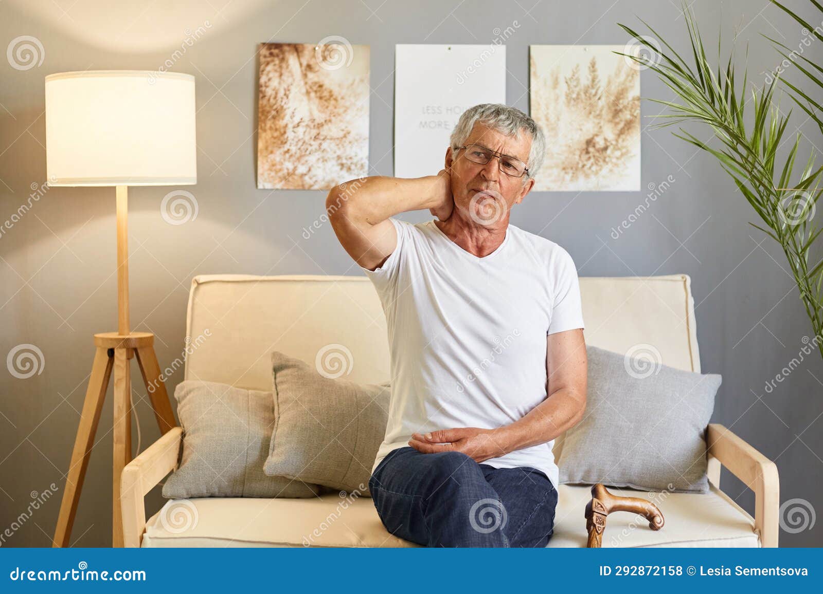 sick ill exhausted grey-haired senior man in casual white t-shirt sitting on couch in uncomfortable pose at home in living room