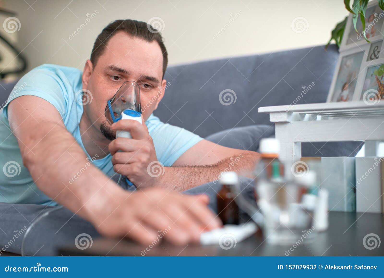 a sick man breathes through an inhaler mask. lying on the couch and pulls his hand to the cure