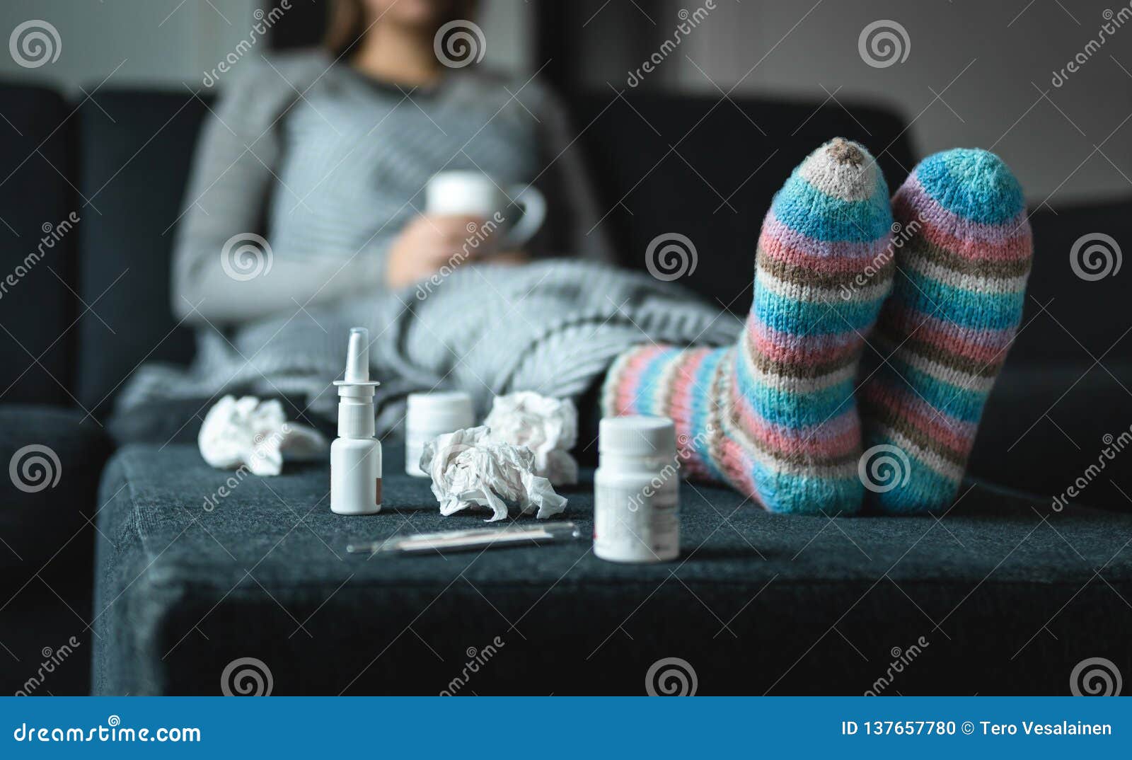 sick woman resting on couch holding hot cup of tea. ill person with flu, cold, fever or virus sitting on sofa at home in winter.