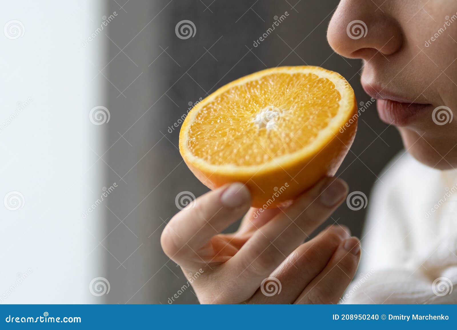 sick woman trying to sense smell of half fresh orange, has symptom of covid-19, loss of smell, taste