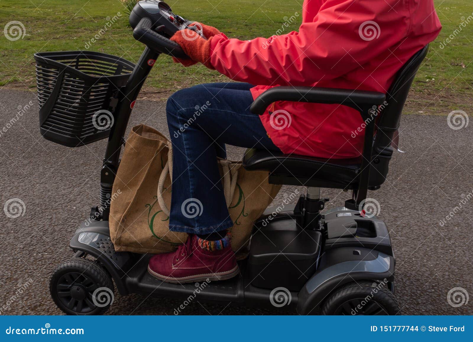 a side on shot of an elderly lady in a red coat enjoying the freedom of an electric mobility scooter