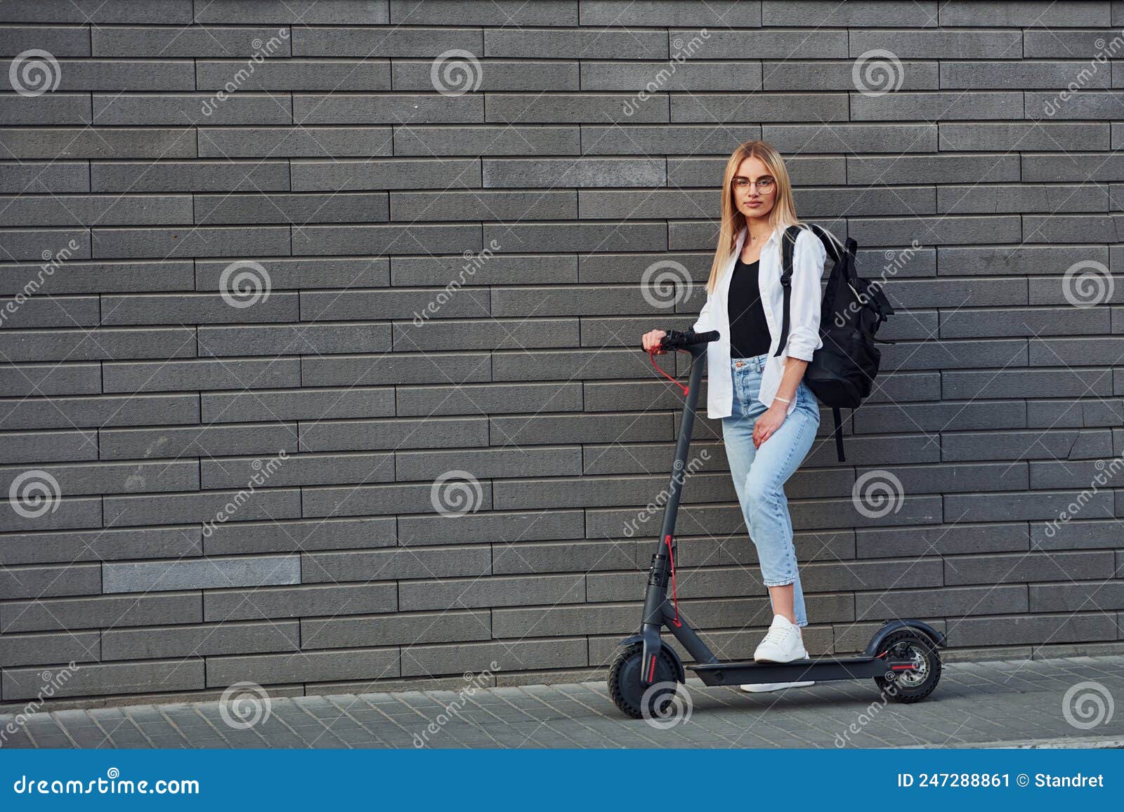 Side View Of Beautiful Blonde In Casual Clothes That Riding Electric Schooter Outdoors At Sunny