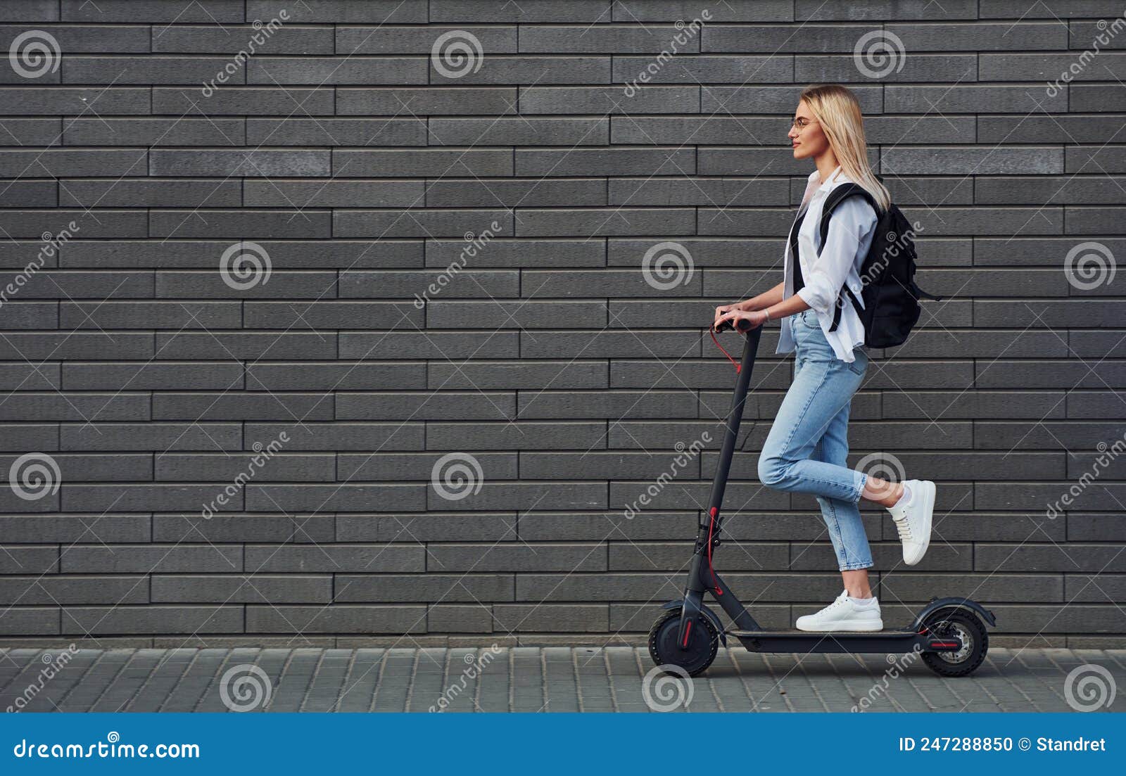 Side View Of Beautiful Blonde In Casual Clothes That Riding Electric Schooter Outdoors At Sunny