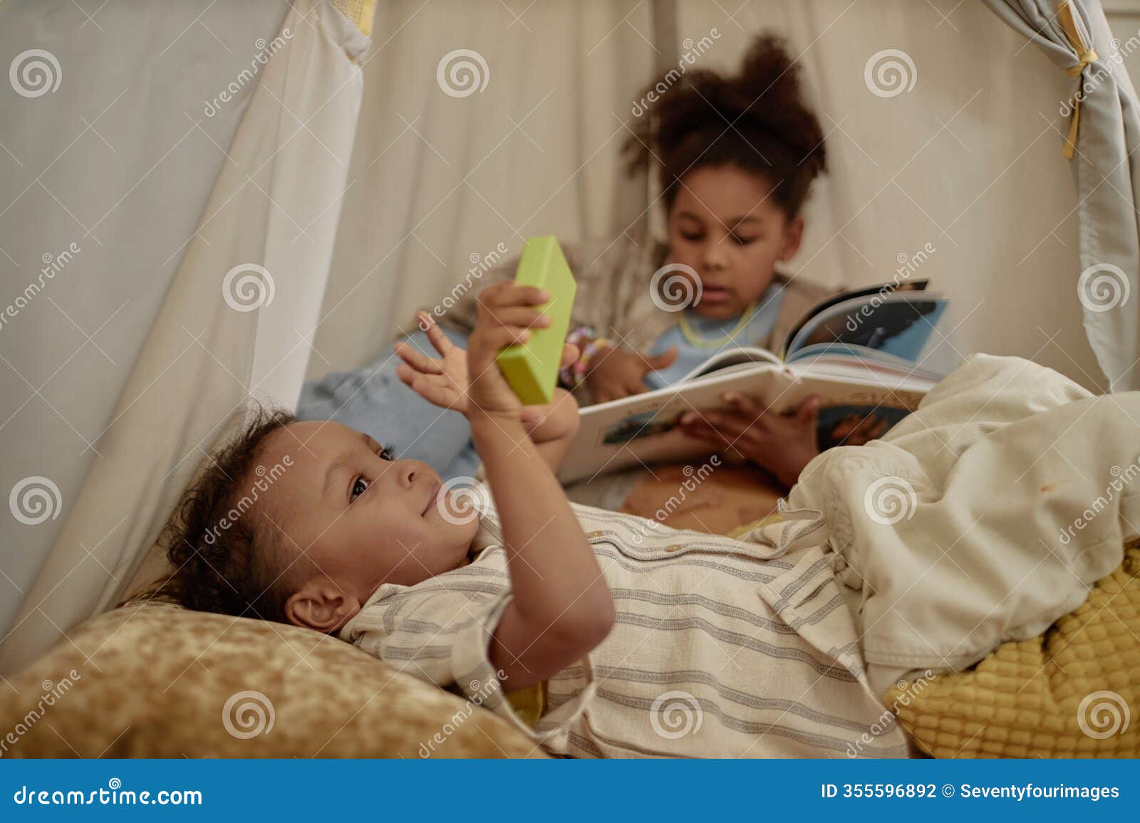 happy little black boy resting inside wigwam while playing with sister at home