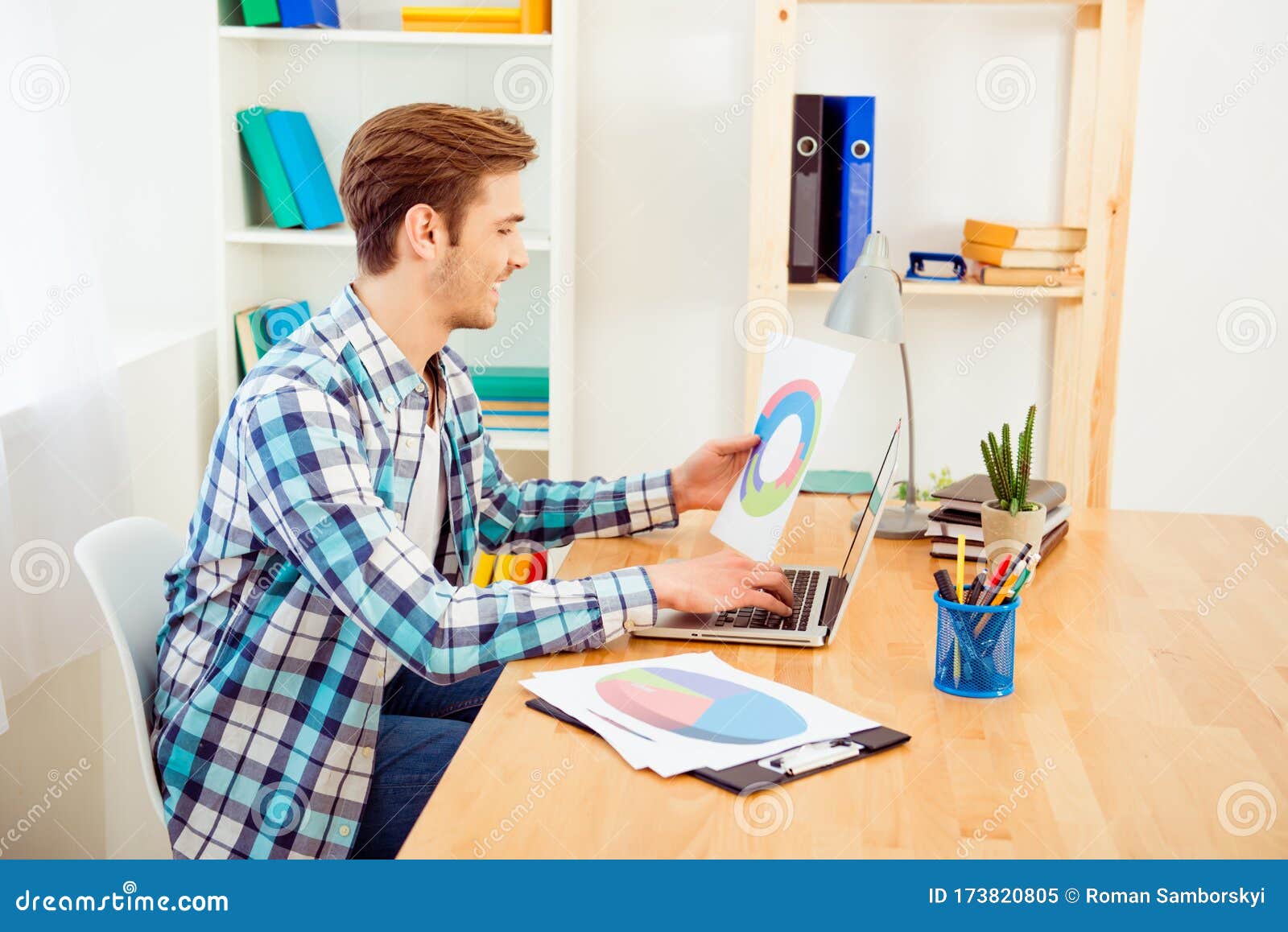 side view of happy worker holding diagrama and typing on laptop