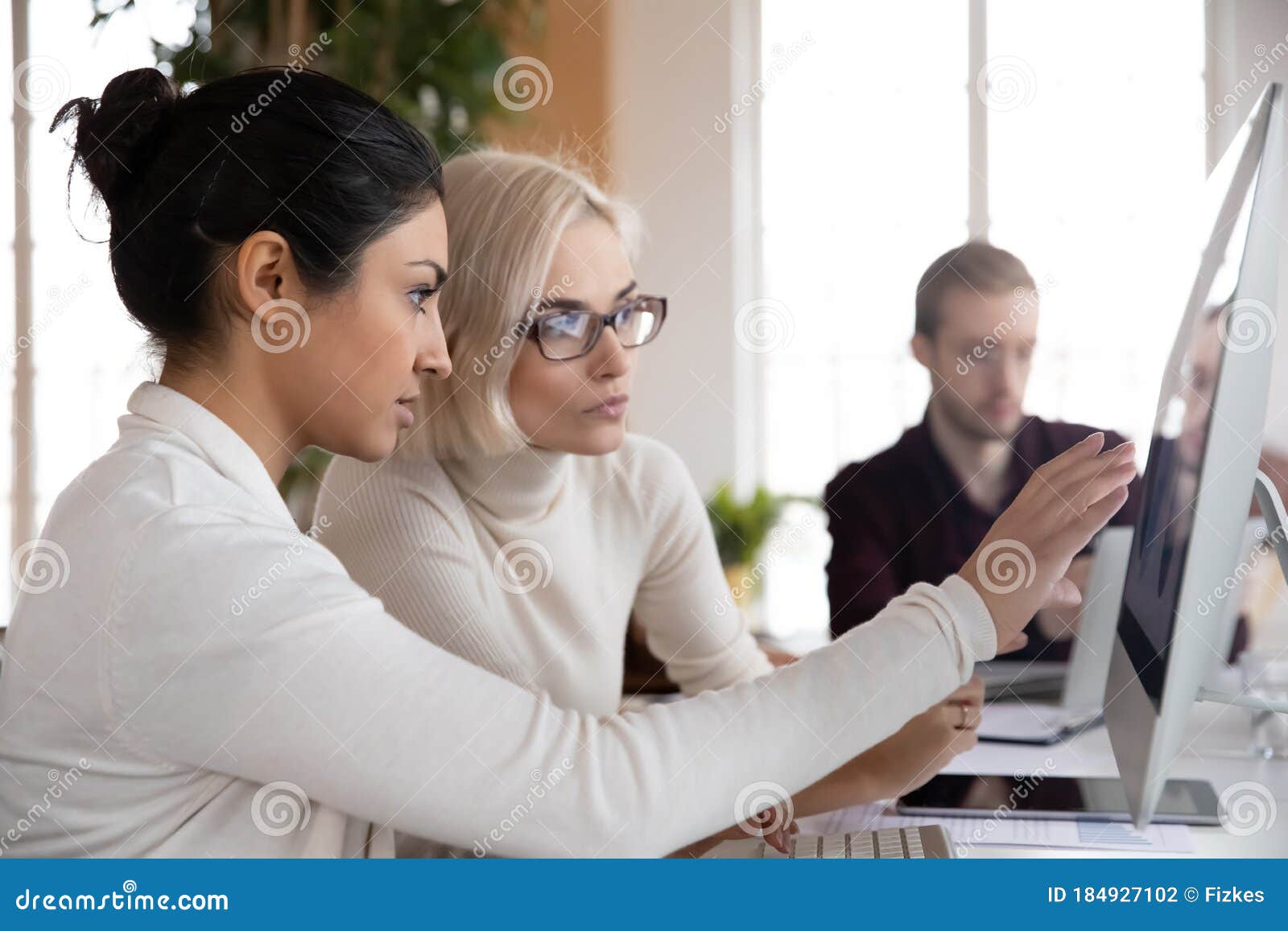 young indian businesswoman working with blonde female colleague on project.